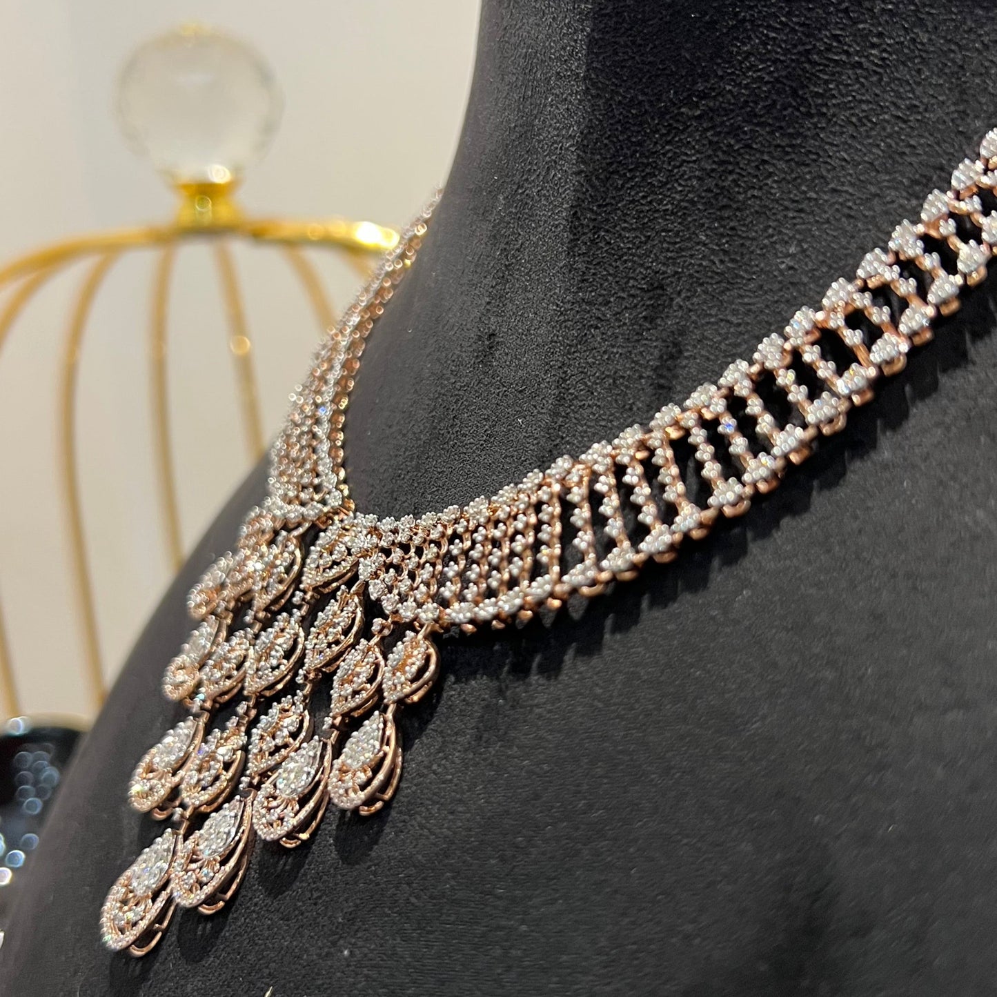 A gold diamond necklace with a geometric pattern and a pair of matching earrings, displayed on a mannequin bust.