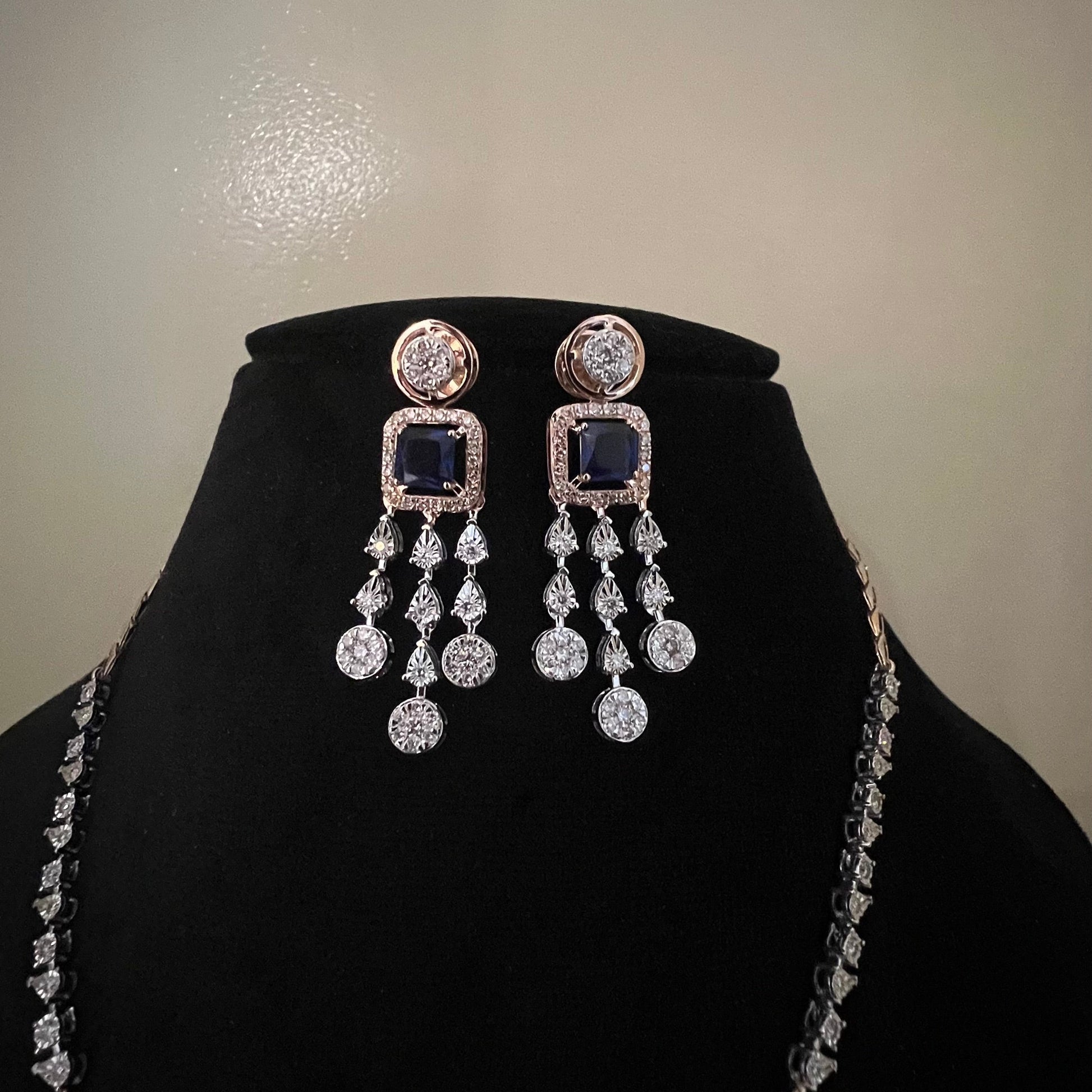 A gold diamond necklace with a matching set of earrings, featuring a series of round and marquise shaped diamonds set in a classic design on a mannequin bust.