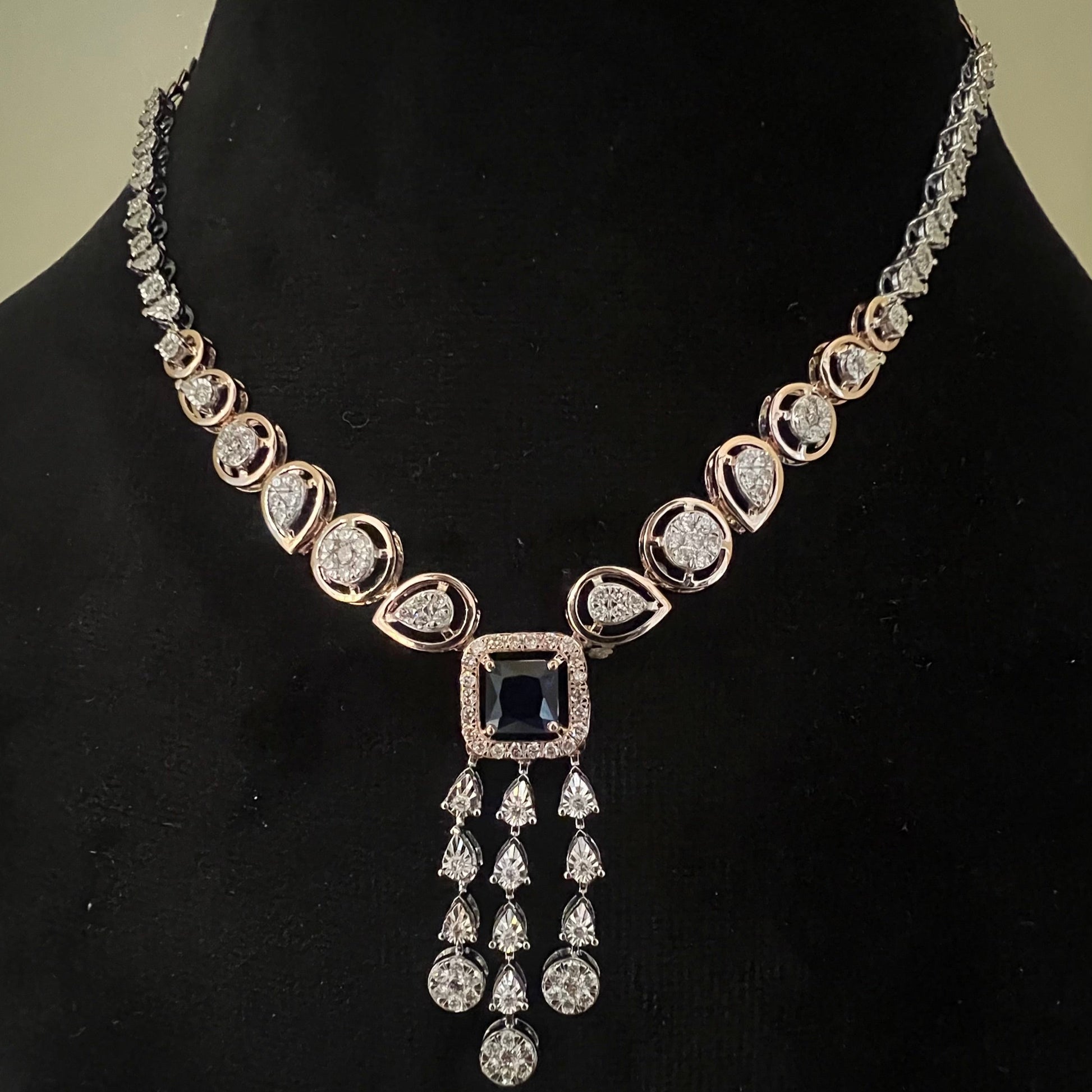 A gold diamond necklace with a matching set of earrings, featuring a series of round and marquise shaped diamonds set in a classic design on a mannequin bust.
