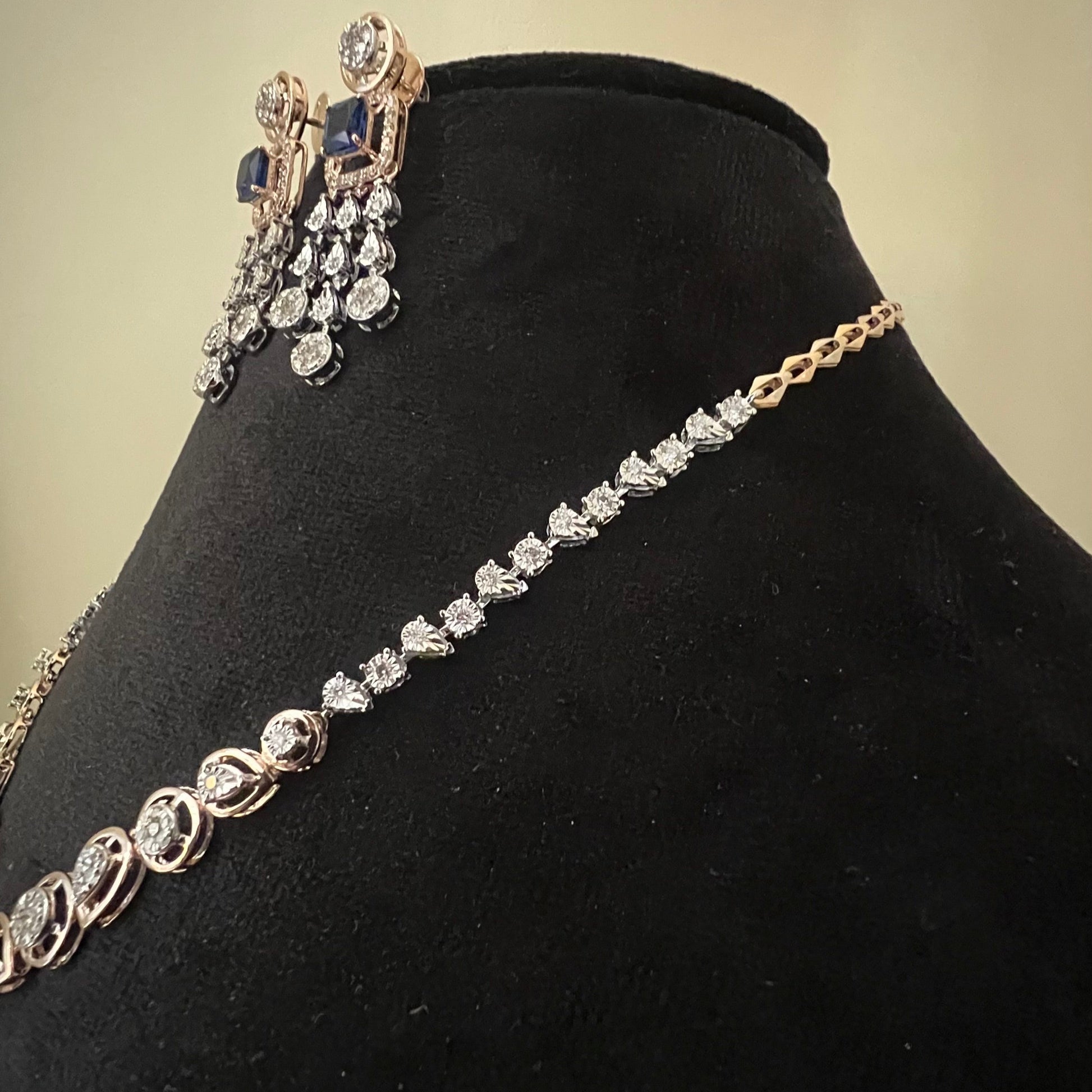 A gold diamond necklace with a matching set of earrings, featuring a series of round and marquise shaped diamonds set in a classic design on a mannequin bust.