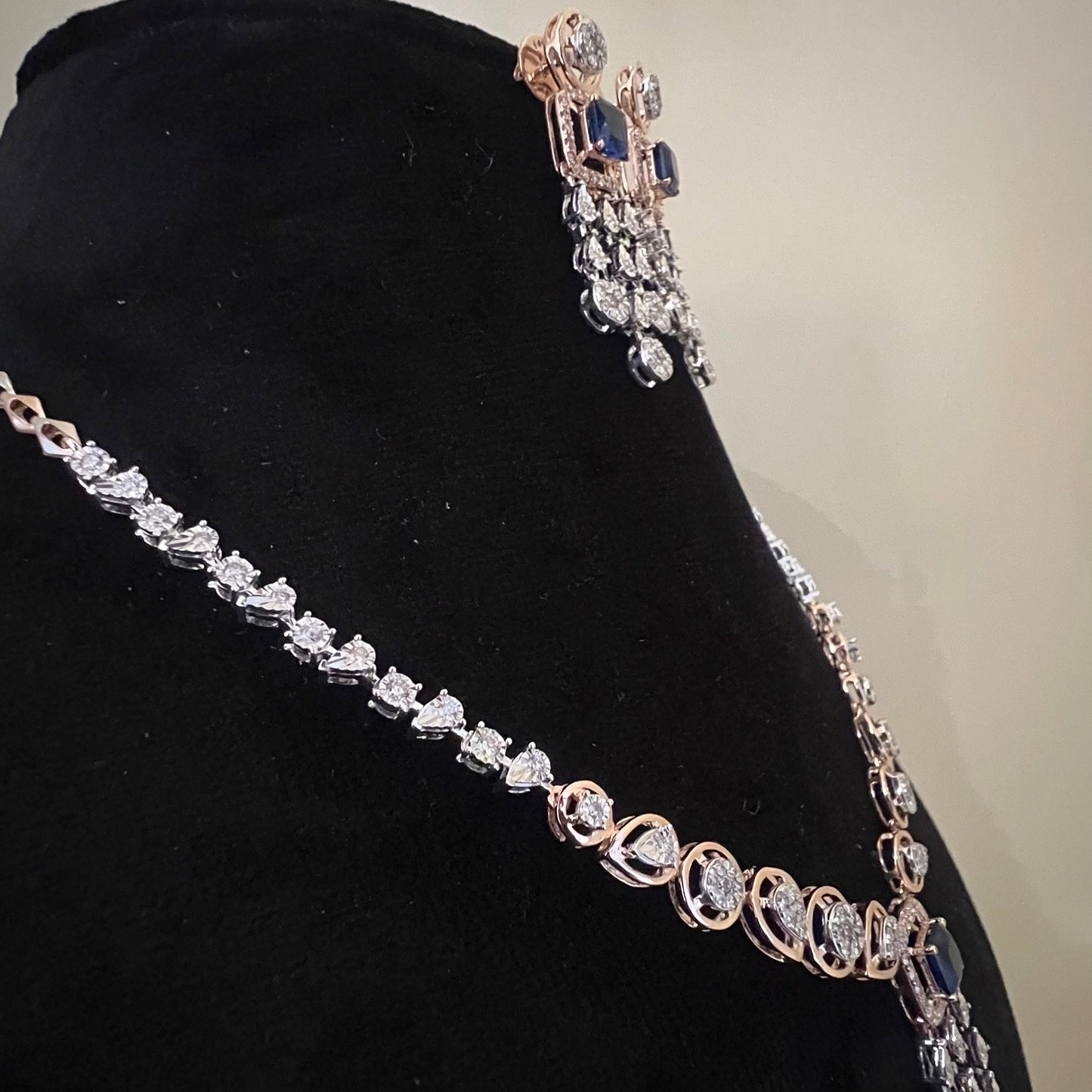 A gold diamond necklace with a matching set of earrings, featuring a series of round and marquise shaped diamonds set in a classic design on a mannequin bust.
