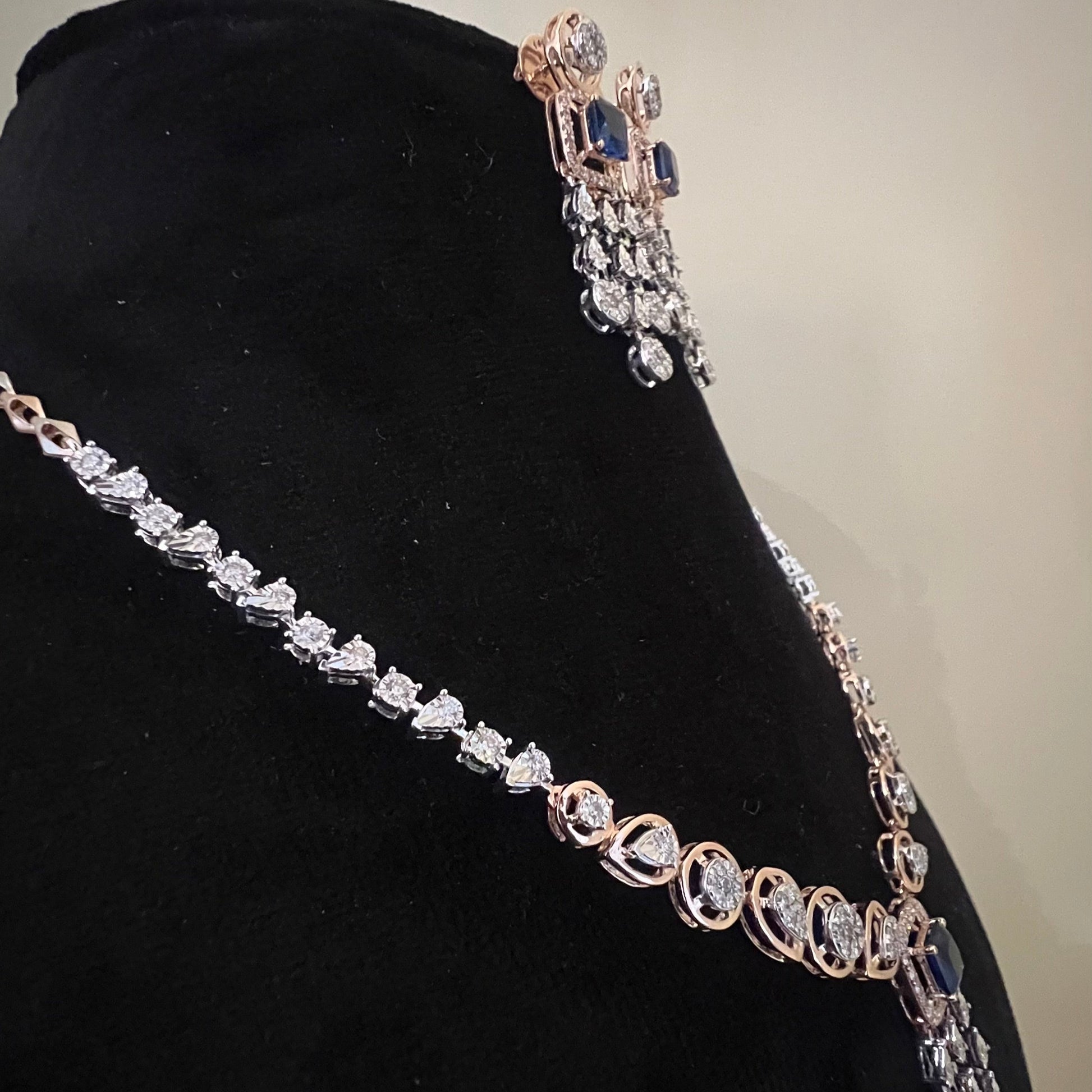 A gold diamond necklace with a matching set of earrings, featuring a series of round and marquise shaped diamonds set in a classic design on a mannequin bust.