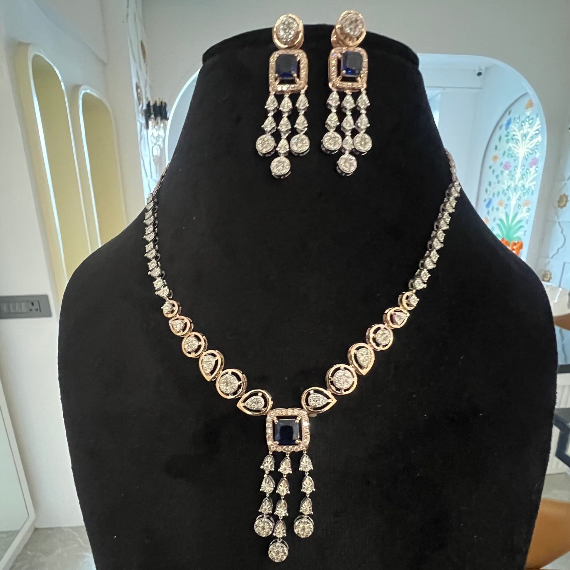 A gold diamond necklace with a matching set of earrings, featuring a series of round and marquise shaped diamonds set in a classic design on a mannequin bust.