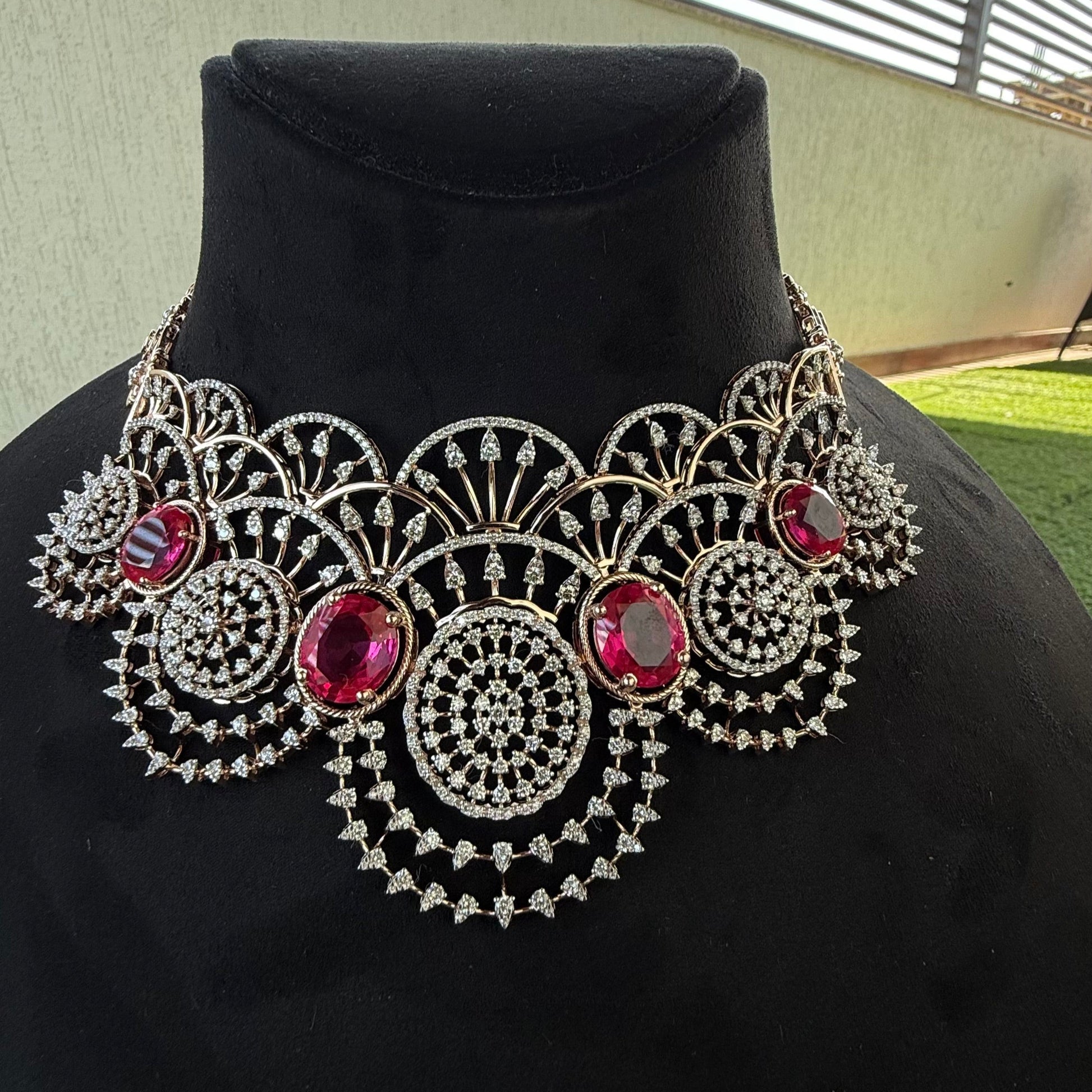 A gold diamond choker necklace with a floral pattern and red and white diamonds, displayed on a mannequin.