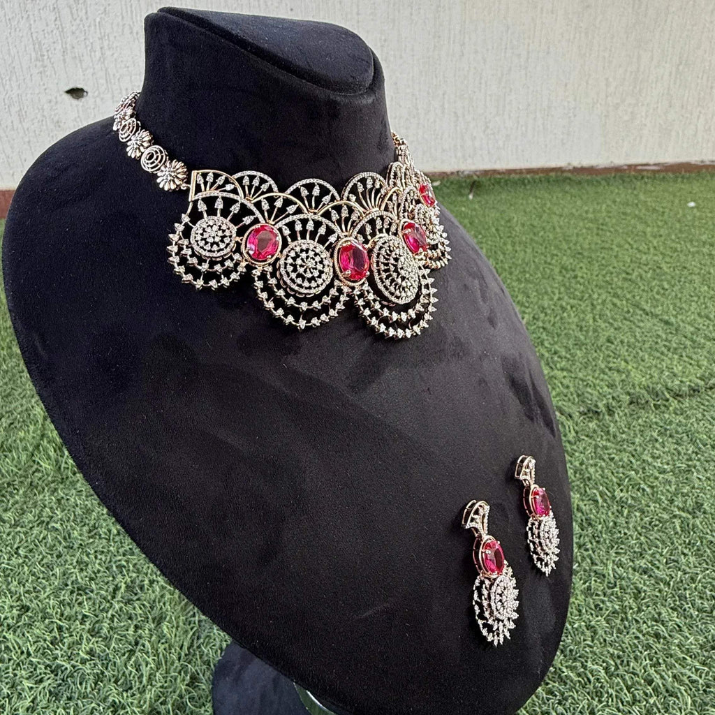 A gold diamond choker necklace with a floral pattern and red and white diamonds, accompanied by matching earrings, displayed on a mannequin.