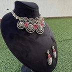 A gold diamond choker necklace with a floral pattern and red and white diamonds, accompanied by matching earrings, displayed on a mannequin.