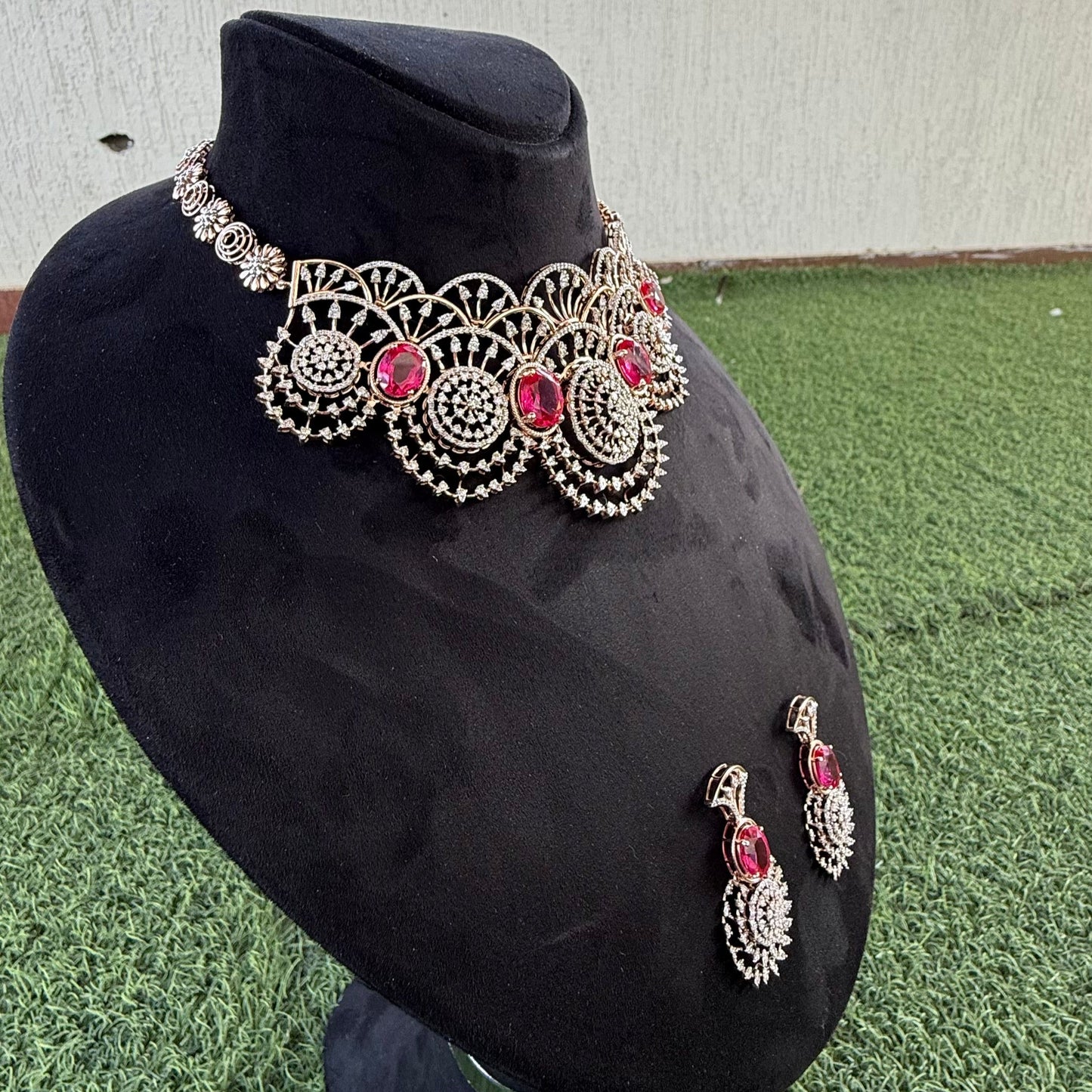 A gold diamond choker necklace with a floral pattern and red and white diamonds, accompanied by matching earrings, displayed on a mannequin.