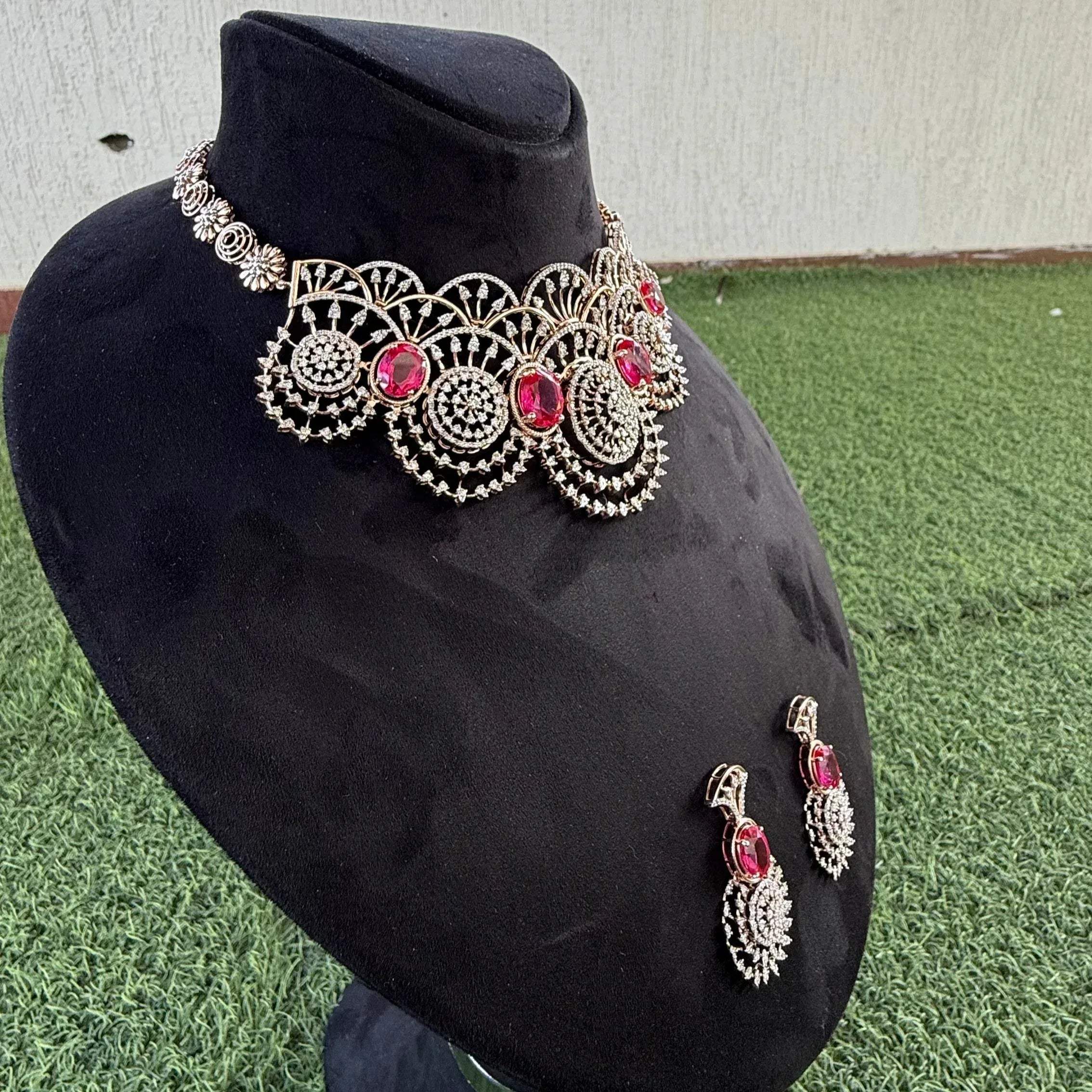 A gold diamond choker necklace with a floral pattern and red and white diamonds, accompanied by matching earrings, displayed on a mannequin.