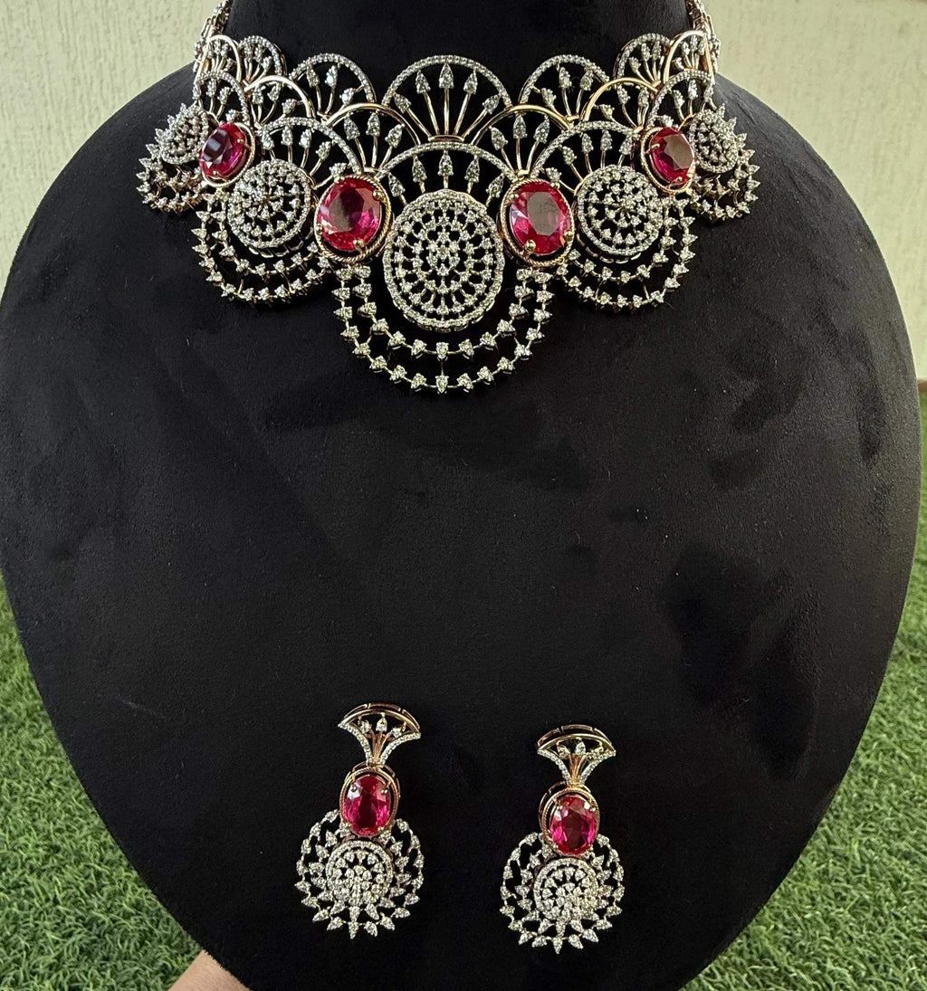 A gold diamond choker necklace with a floral pattern and red and white diamonds, accompanied by matching earrings, displayed on a mannequin.
