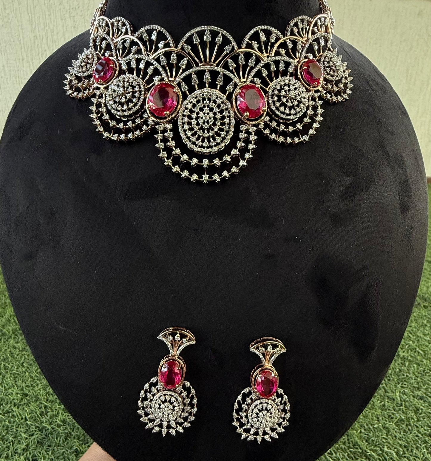 A gold diamond choker necklace with a floral pattern and red and white diamonds, accompanied by matching earrings, displayed on a mannequin.