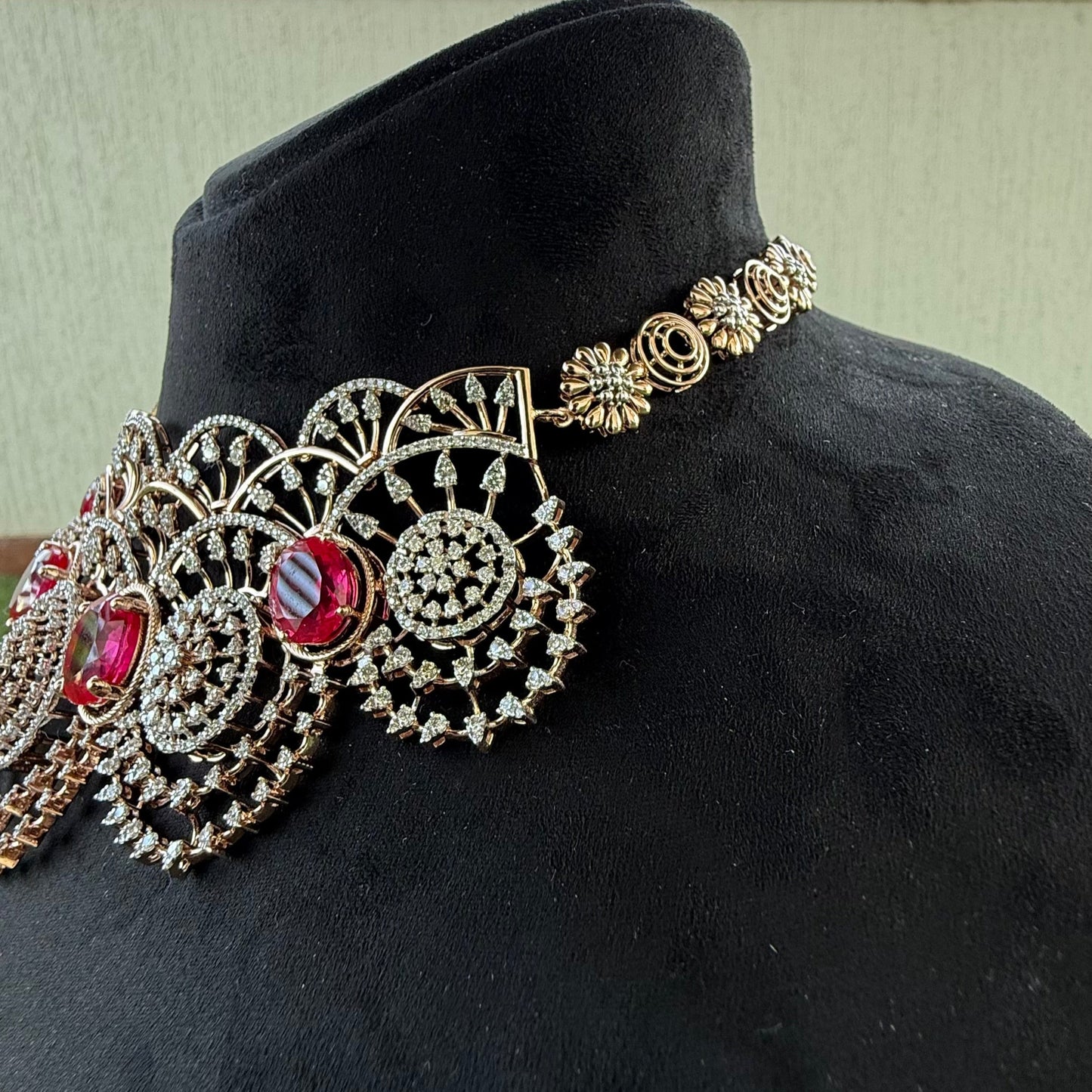 A gold diamond choker necklace with a floral pattern and red and white diamonds, displayed on a mannequin from left side.