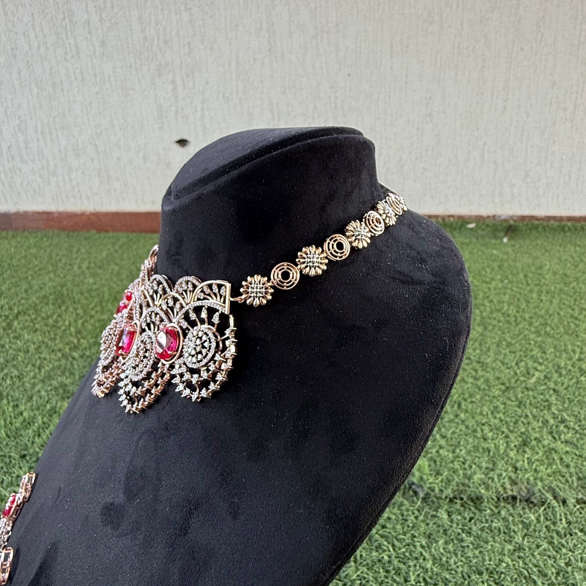 A gold diamond choker necklace with a floral pattern and red and white diamonds, displayed on a mannequin.