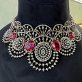 A gold diamond choker necklace with a floral pattern and red and white diamonds, accompanied by matching earrings, displayed on a mannequin.