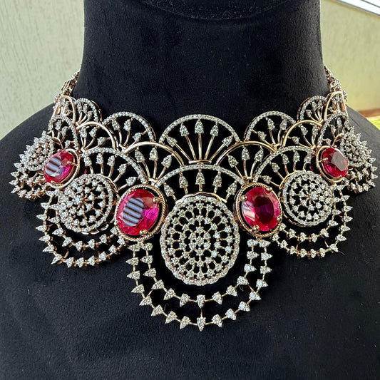 A gold diamond choker necklace with a floral pattern and red and white diamonds, accompanied by matching earrings, displayed on a mannequin.