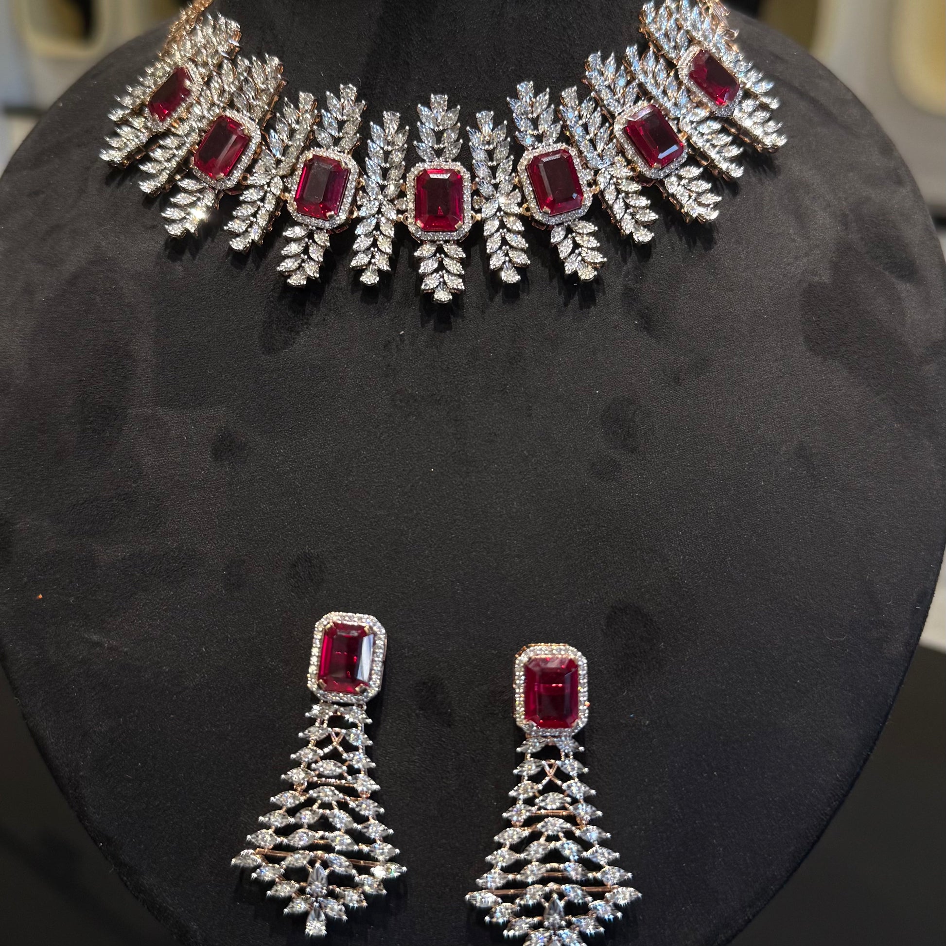 Diamond necklace set with emerald-cut color stones and leaf-shaped diamond clusters, paired with matching color stone and diamond earrings is displayed on a mannequin.