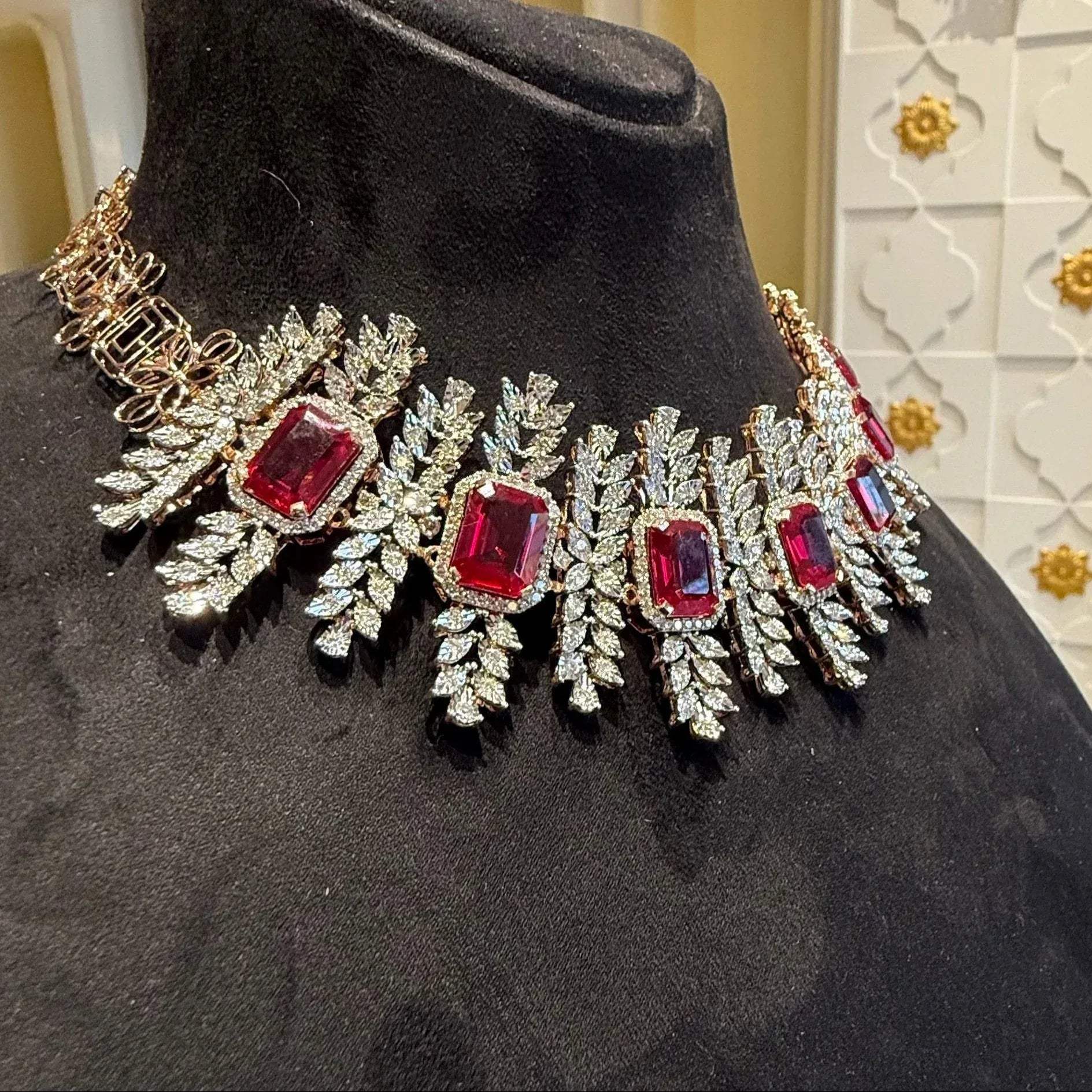 Diamond necklace set with emerald-cut color stones and leaf-shaped diamond clusters is displayed on a mannequin from right side.