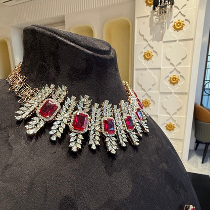 Diamond necklace set with emerald-cut color stones and leaf-shaped diamond clusters is displayed on a mannequin from right side.