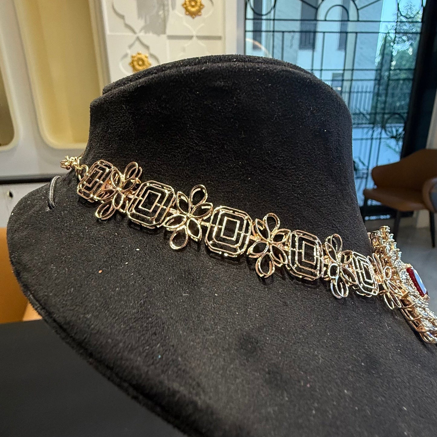Diamond necklace set with emerald-cut color stones and leaf-shaped diamond clusters is displayed on a mannequin from back side.