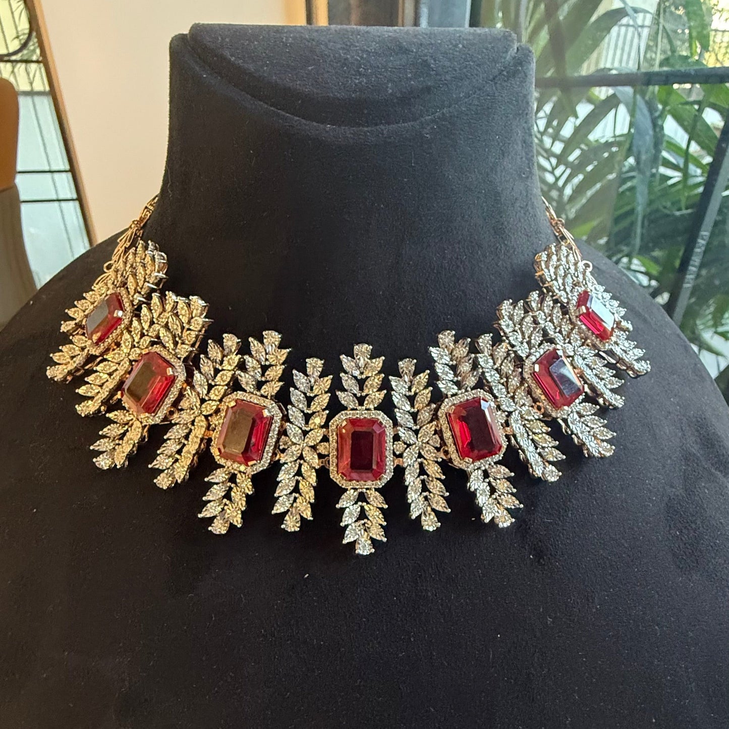 Diamond necklace set with emerald-cut color stones and leaf-shaped diamond clusters is displayed on a mannequin from front side.