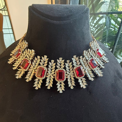 Diamond necklace set with emerald-cut color stones and leaf-shaped diamond clusters is displayed on a mannequin from front side.
