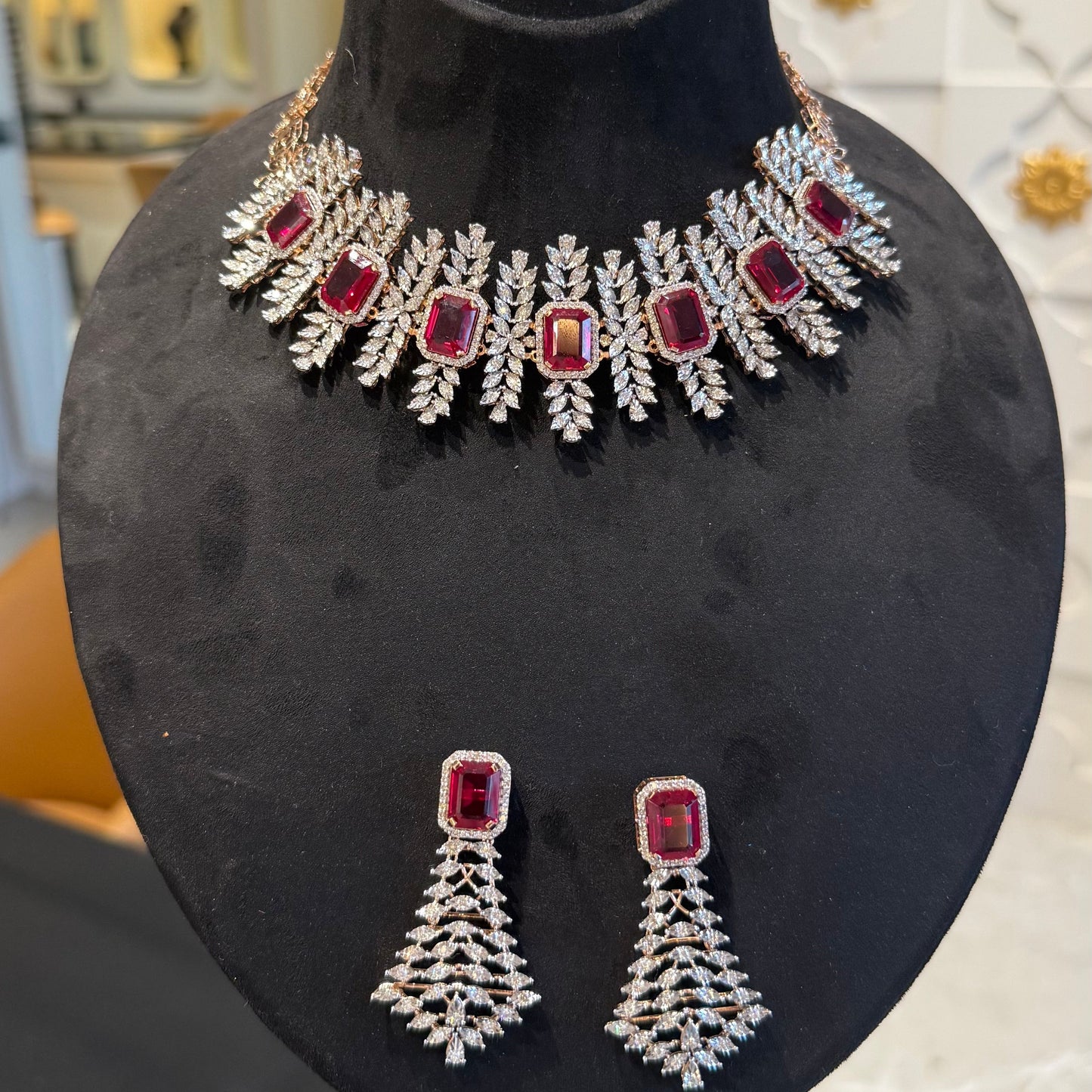 Diamond necklace set with emerald-cut color stones and leaf-shaped diamond clusters, paired with matching color stone and diamond earrings is displayed on a mannequin.