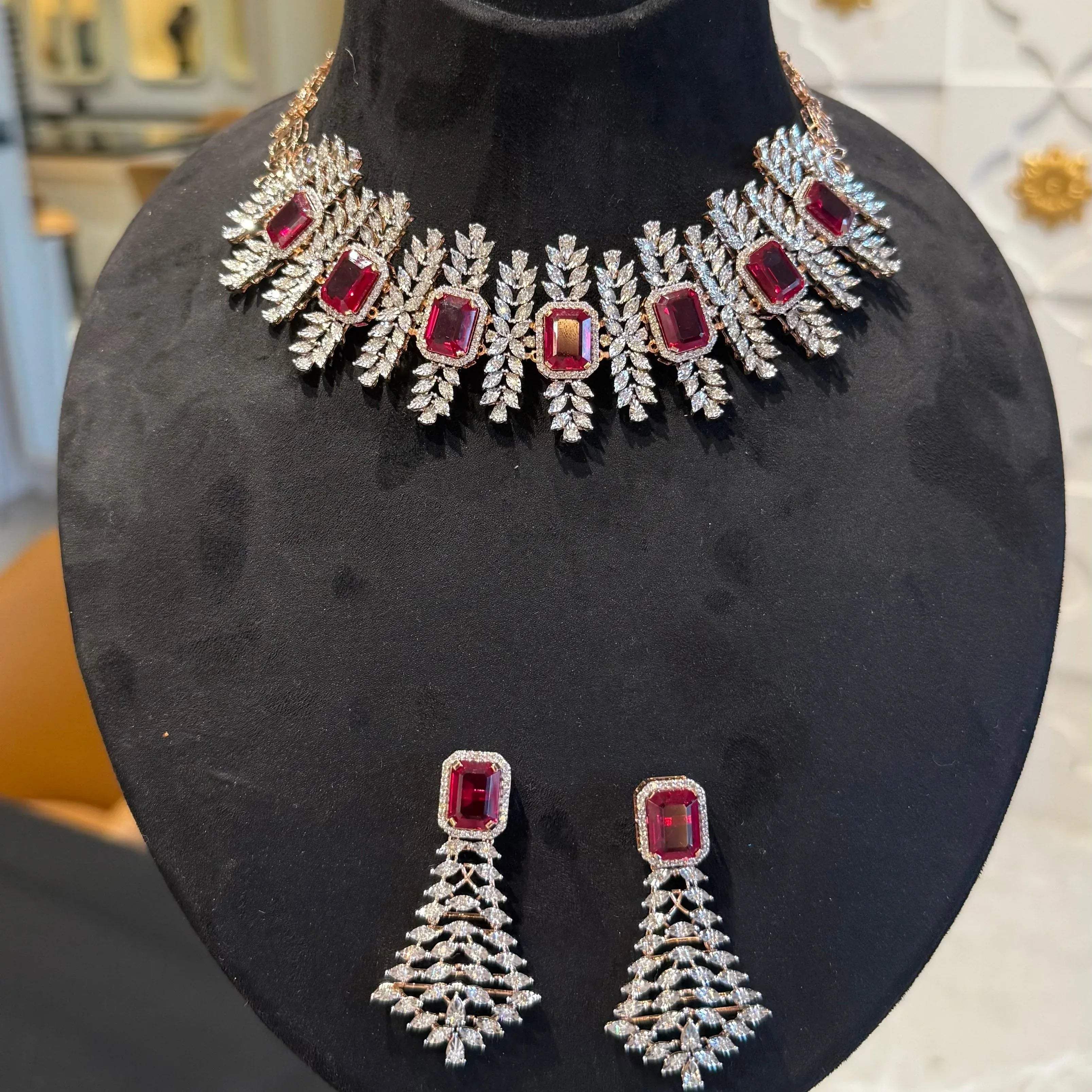 Diamond necklace set with emerald-cut color stones and leaf-shaped diamond clusters, paired with matching color stone and diamond earrings is displayed on a mannequin.