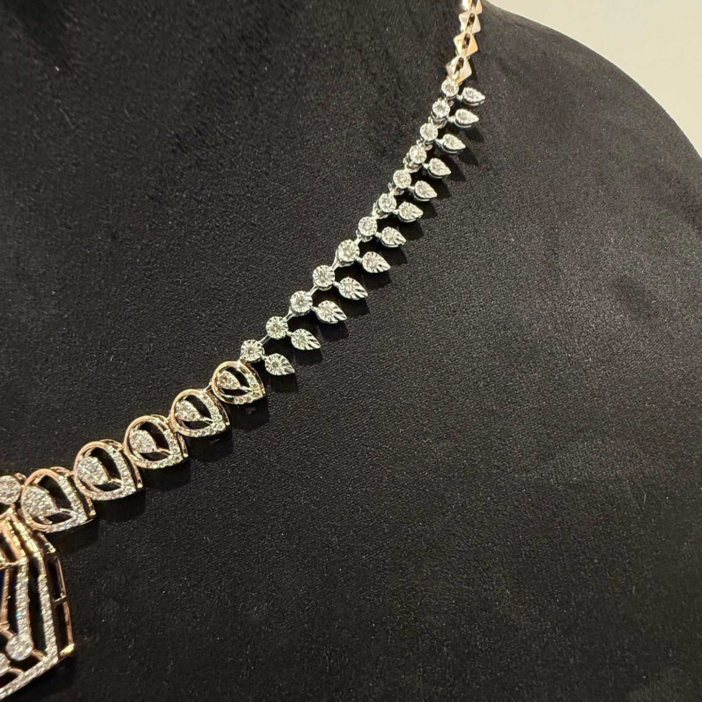 A gold diamond necklace with a geometric pendant displayed on a mannequin bust.