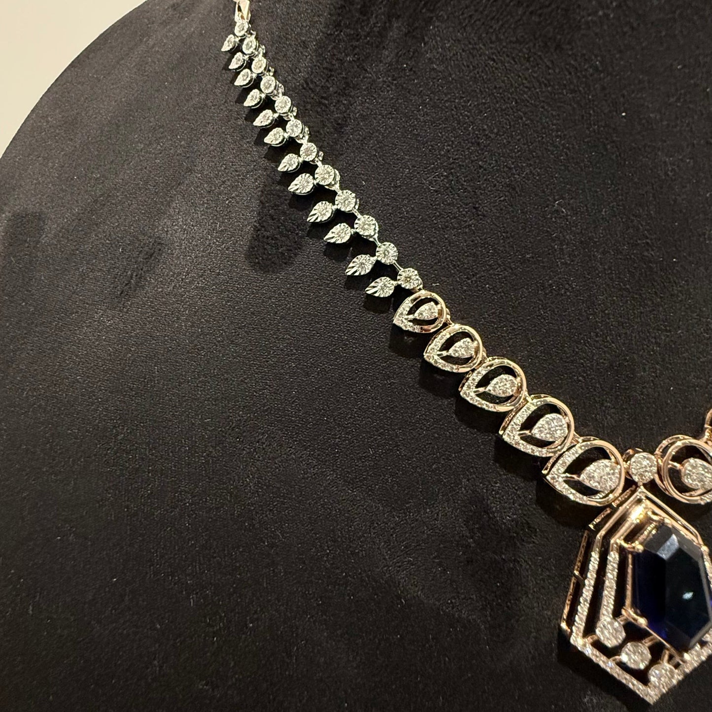 A gold diamond necklace with a geometric pendant displayed on a mannequin bust.