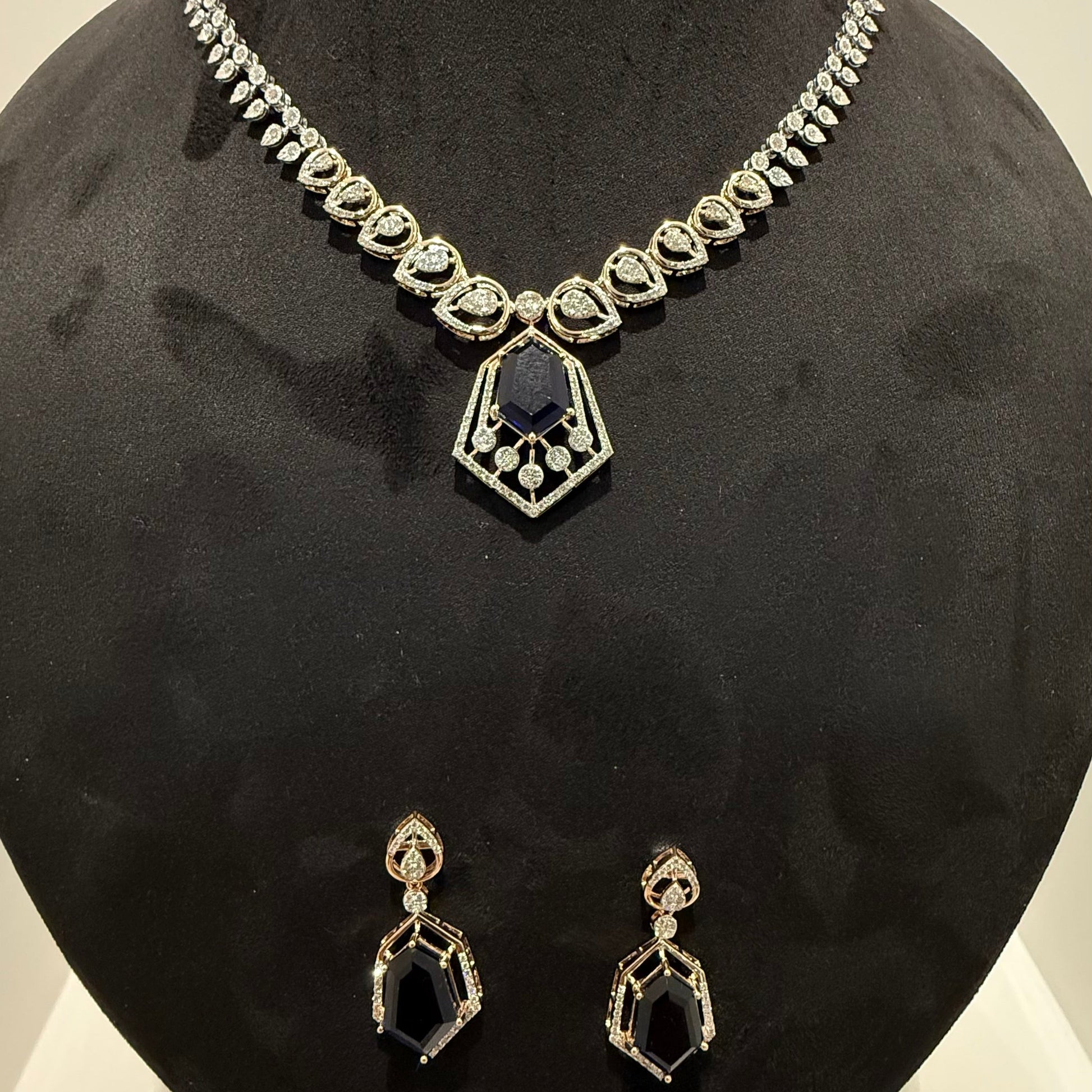 A gold diamond necklace with a geometric pendant and matching earrings displayed on a mannequin bust.