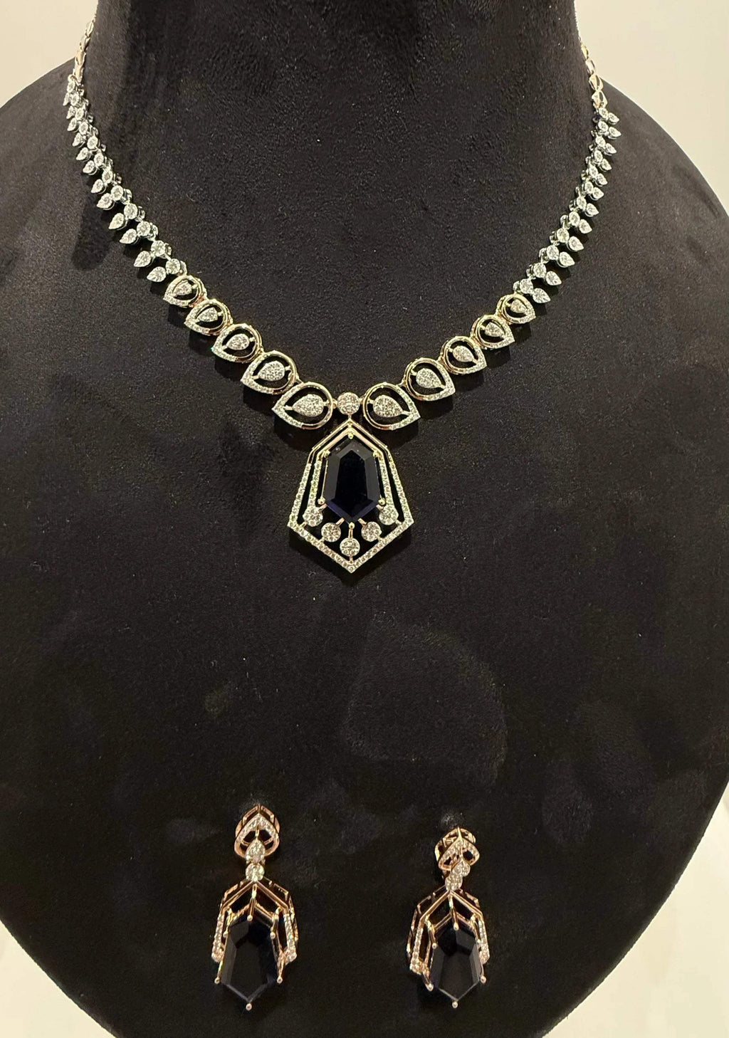 A gold diamond necklace with a geometric pendant and matching earrings displayed on a mannequin bust.