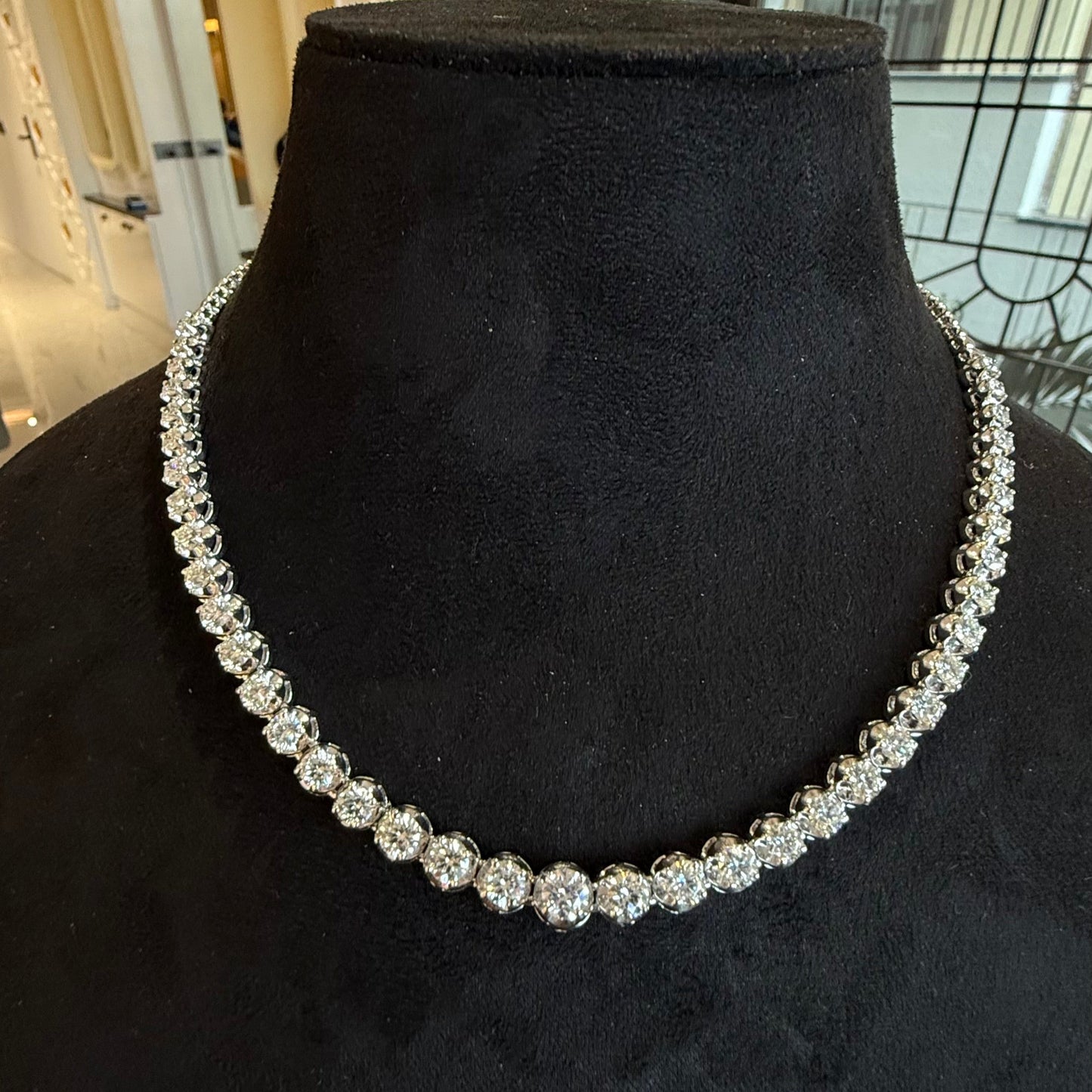 Elegant round cut diamond necklace set displayed on a black mannequin stand.