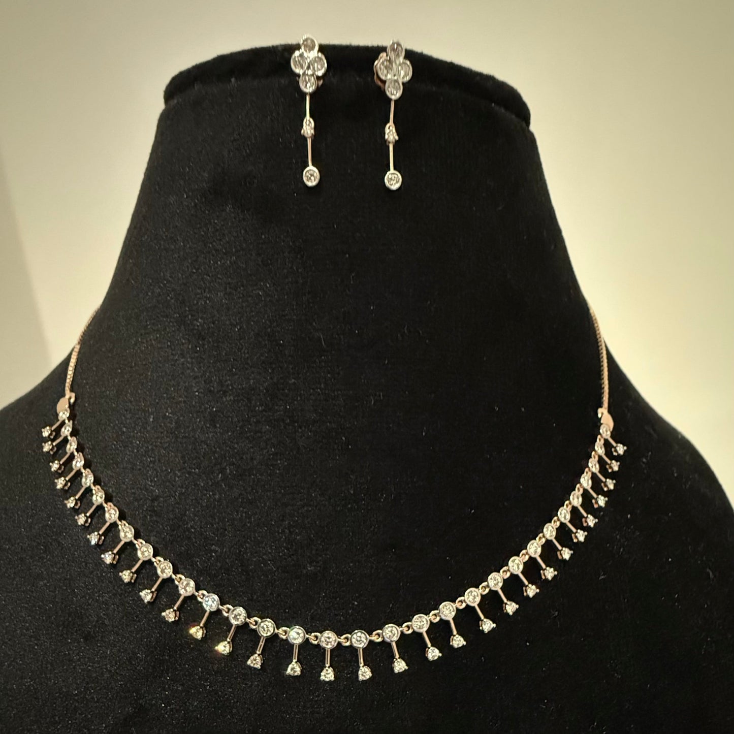 A mannequin showcasing a minimalist diamond necklace and earrings set in gold.