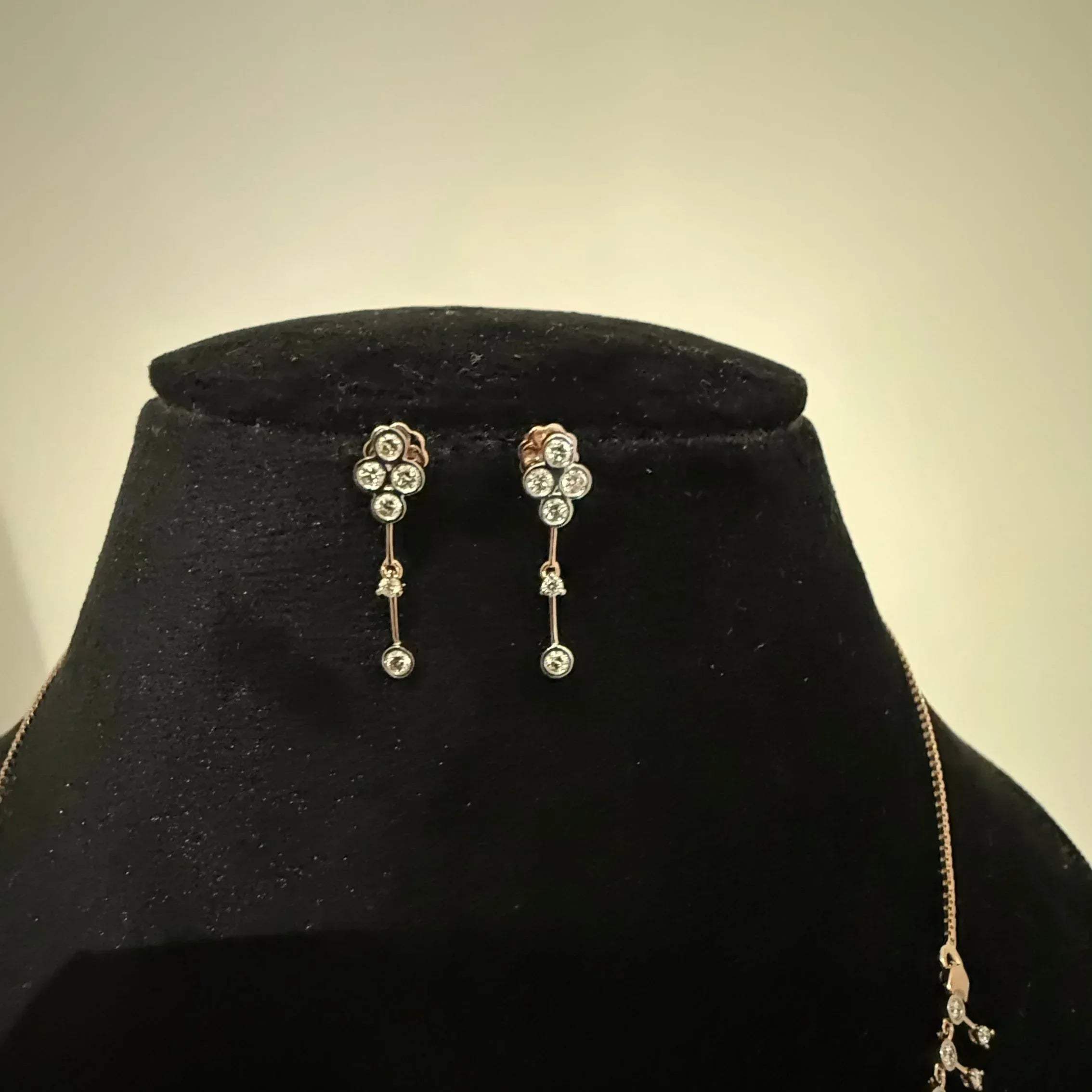 A mannequin showcasing a minimalist diamond necklace and earrings set in gold.