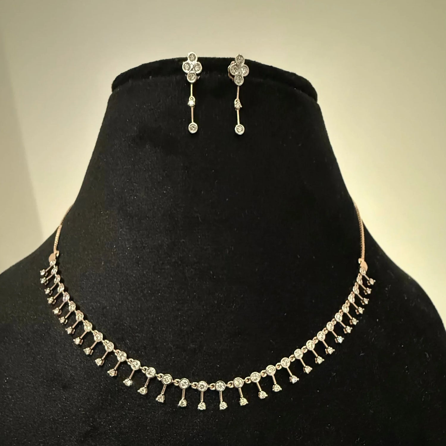 A mannequin showcasing a minimalist diamond necklace and earrings set in gold.