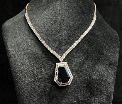 A diamond necklace set featuring a striking geometric deep blue gemstone pendant, all displayed on a black velvet background.