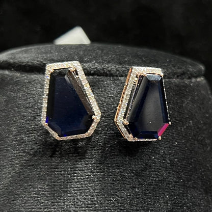 A diamond earrings set featuring a striking geometric deep blue gemstone, all displayed on a black velvet background.