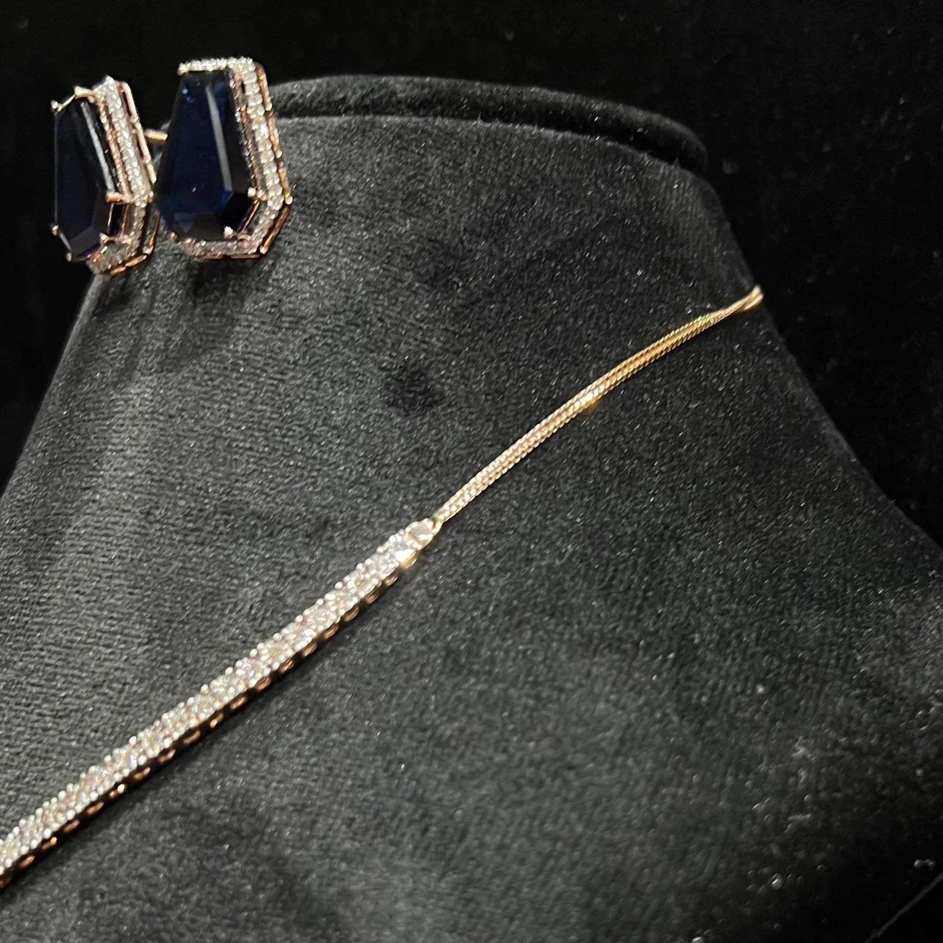 A diamond necklace set featuring a striking geometric deep blue gemstone with matching earrings, all displayed on a black velvet background from left side.