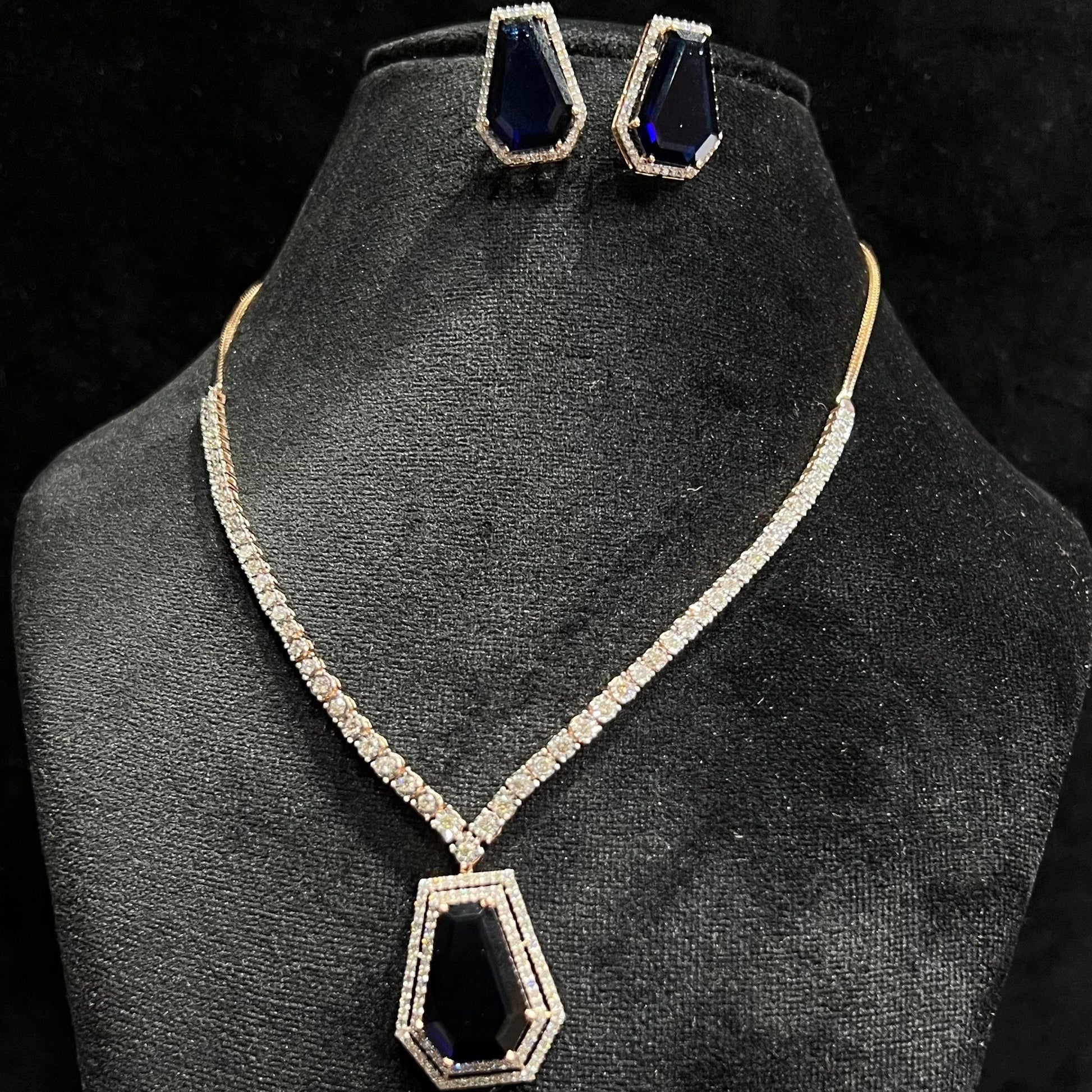 A diamond necklace set featuring a striking geometric deep blue gemstone pendant with matching earrings, all displayed on a black velvet background.