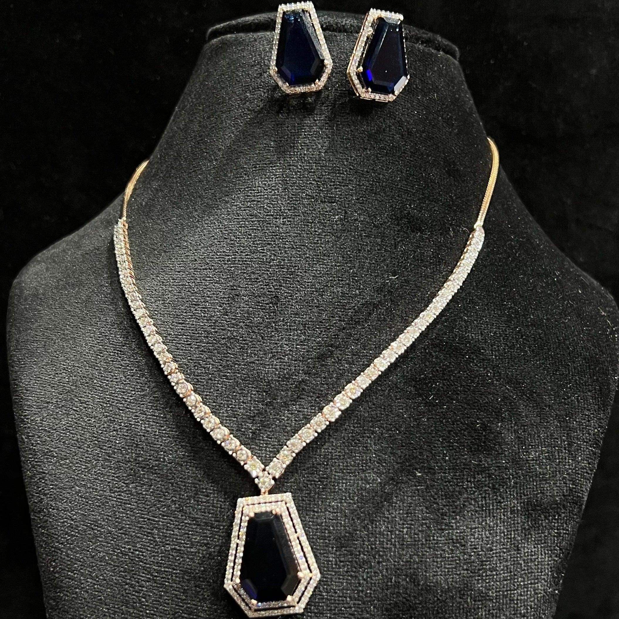 A diamond necklace set featuring a striking geometric deep blue gemstone pendant with matching earrings, all displayed on a black velvet background.
