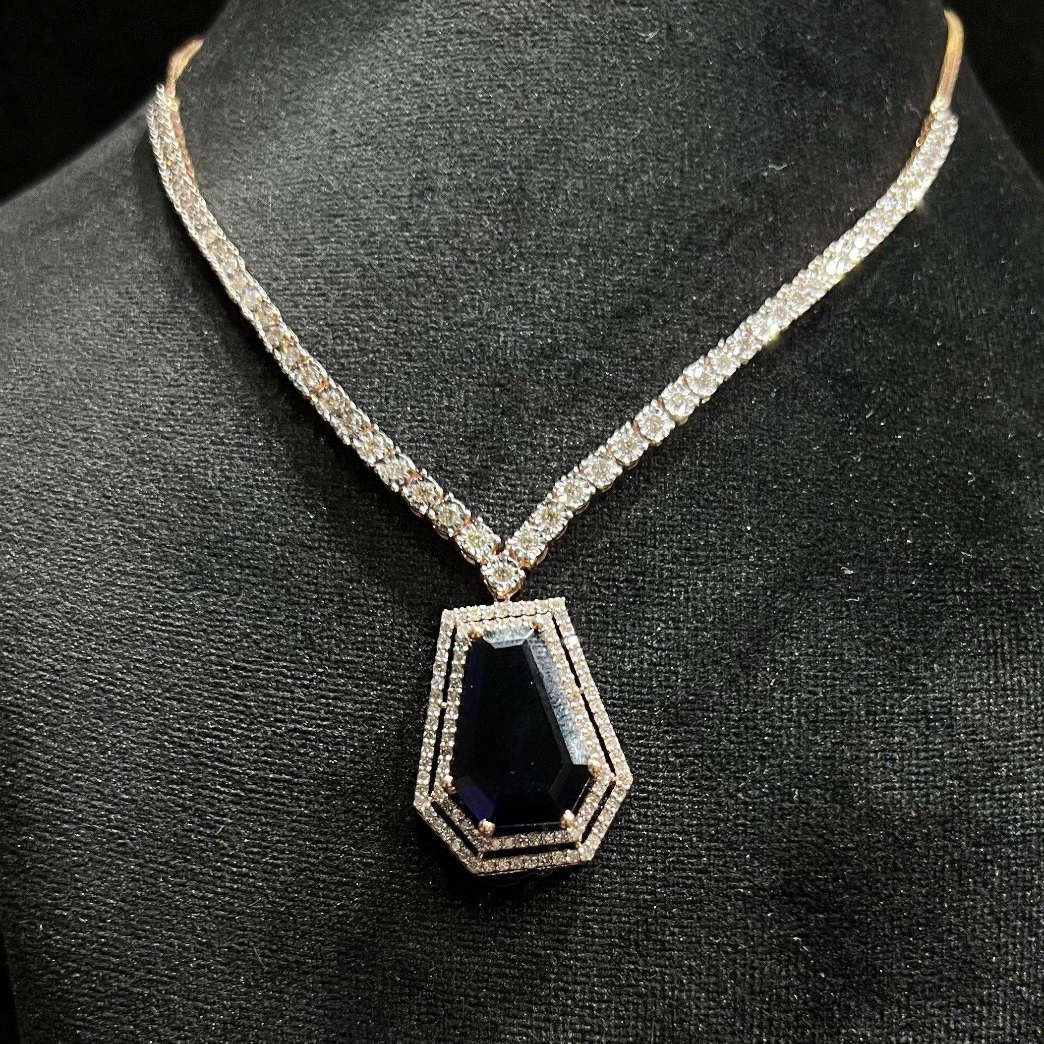 A diamond necklace set featuring a striking geometric deep blue gemstone pendant, all displayed on a black velvet background.