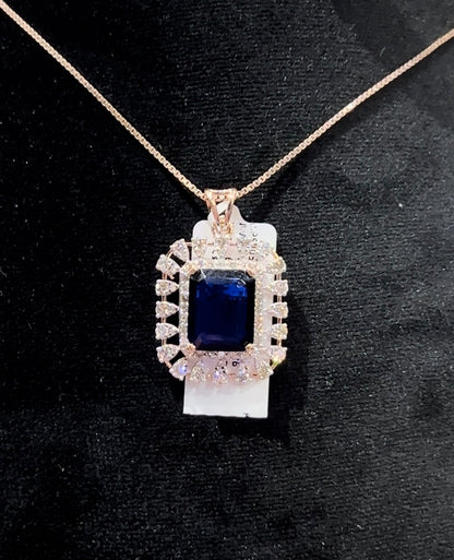 A gold diamond pendant with a blue center stone surrounded by smaller white diamonds, attached to a gold chain for earrings.