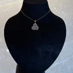A gold diamond pendant with a floral design, displayed on a black mannequin necklace stand.