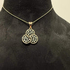 A gold diamond pendant with a floral design, displayed on a black mannequin necklace stand.