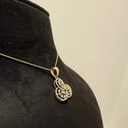 A gold diamond pendant with a floral design, displayed on a black mannequin necklace stand.