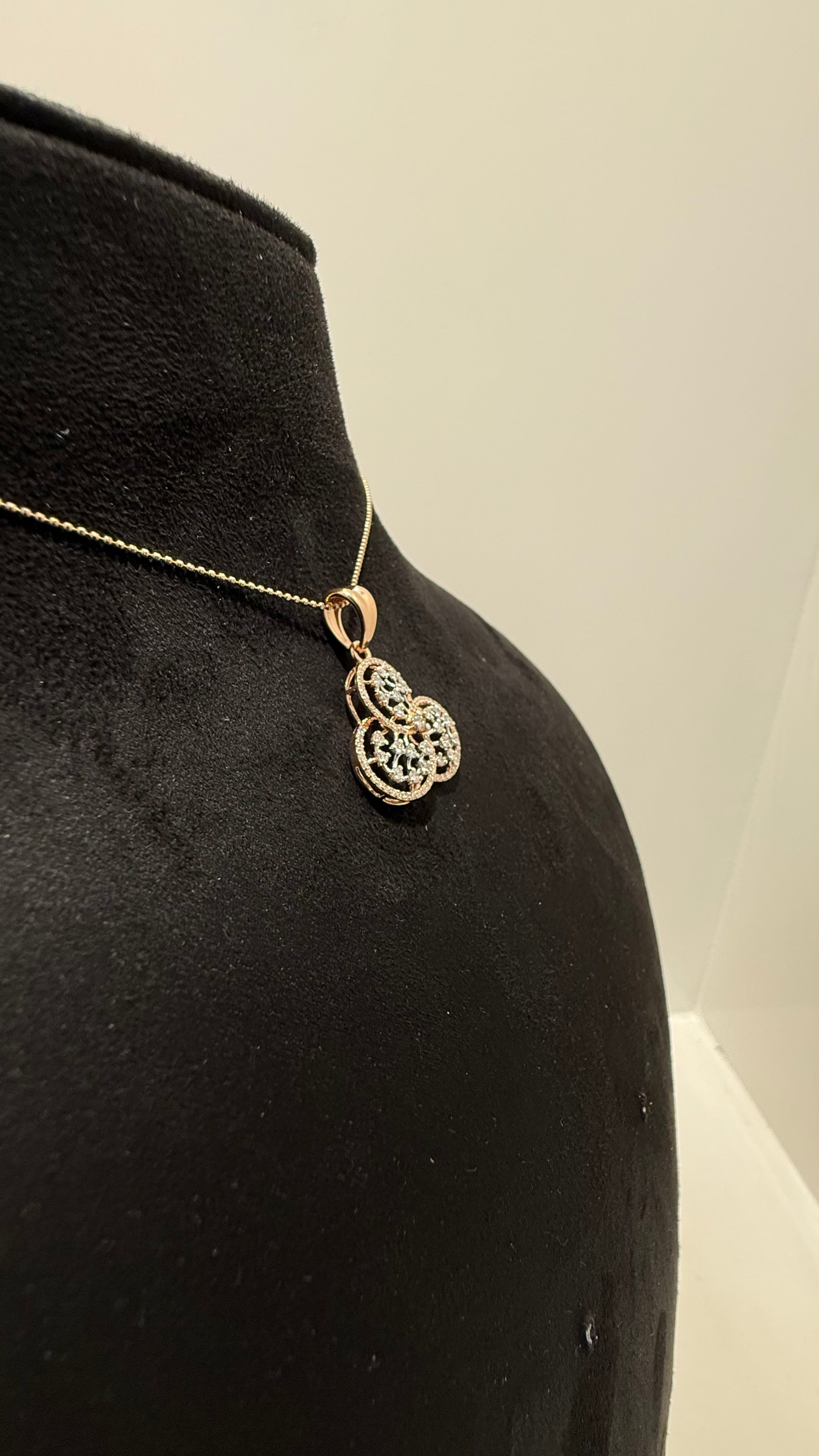 A gold diamond pendant with a floral design, displayed on a black mannequin necklace stand.