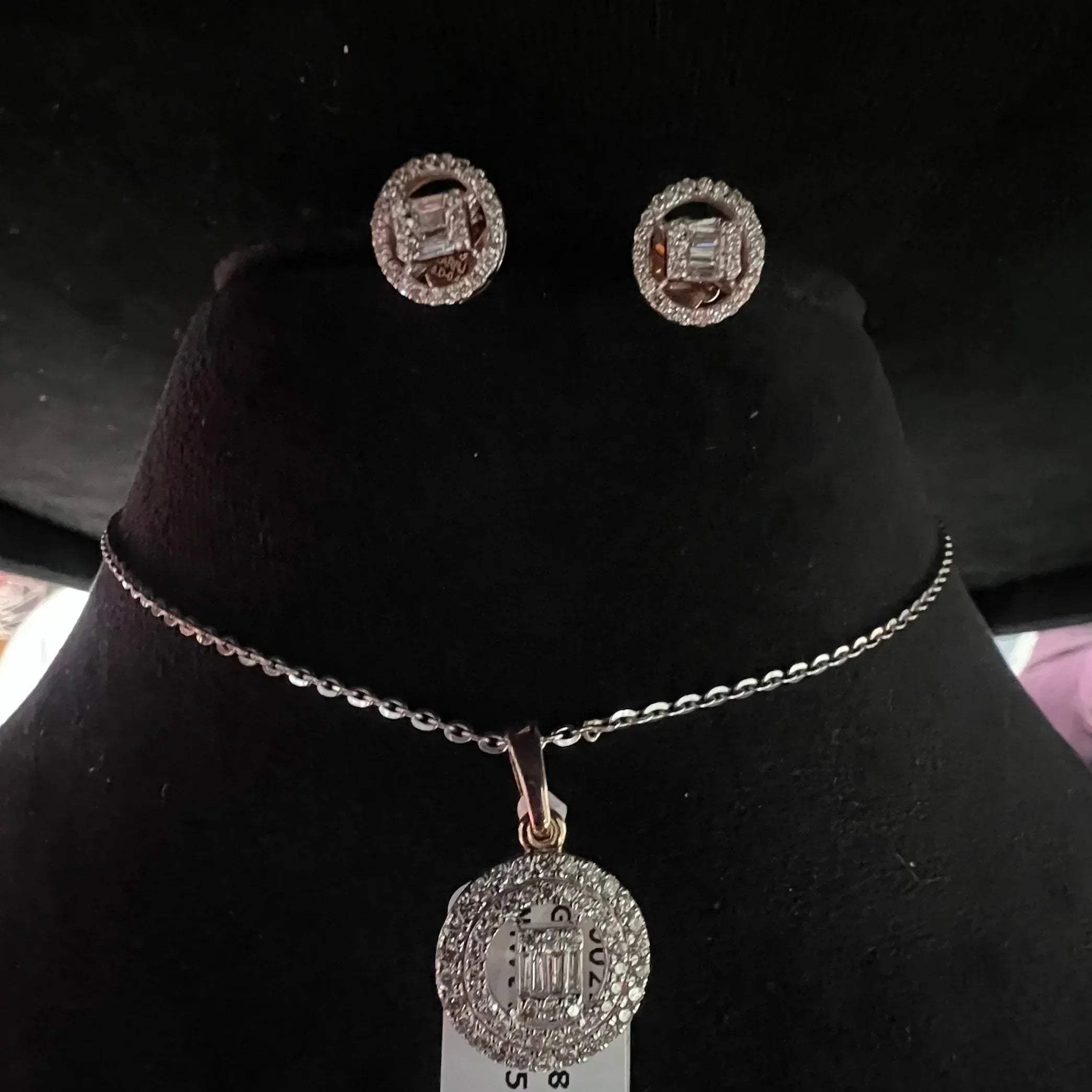 A mannequin showcasing a gold diamond pendant and earrings set, with the pendant hanging from a chain and the earrings displayed above.