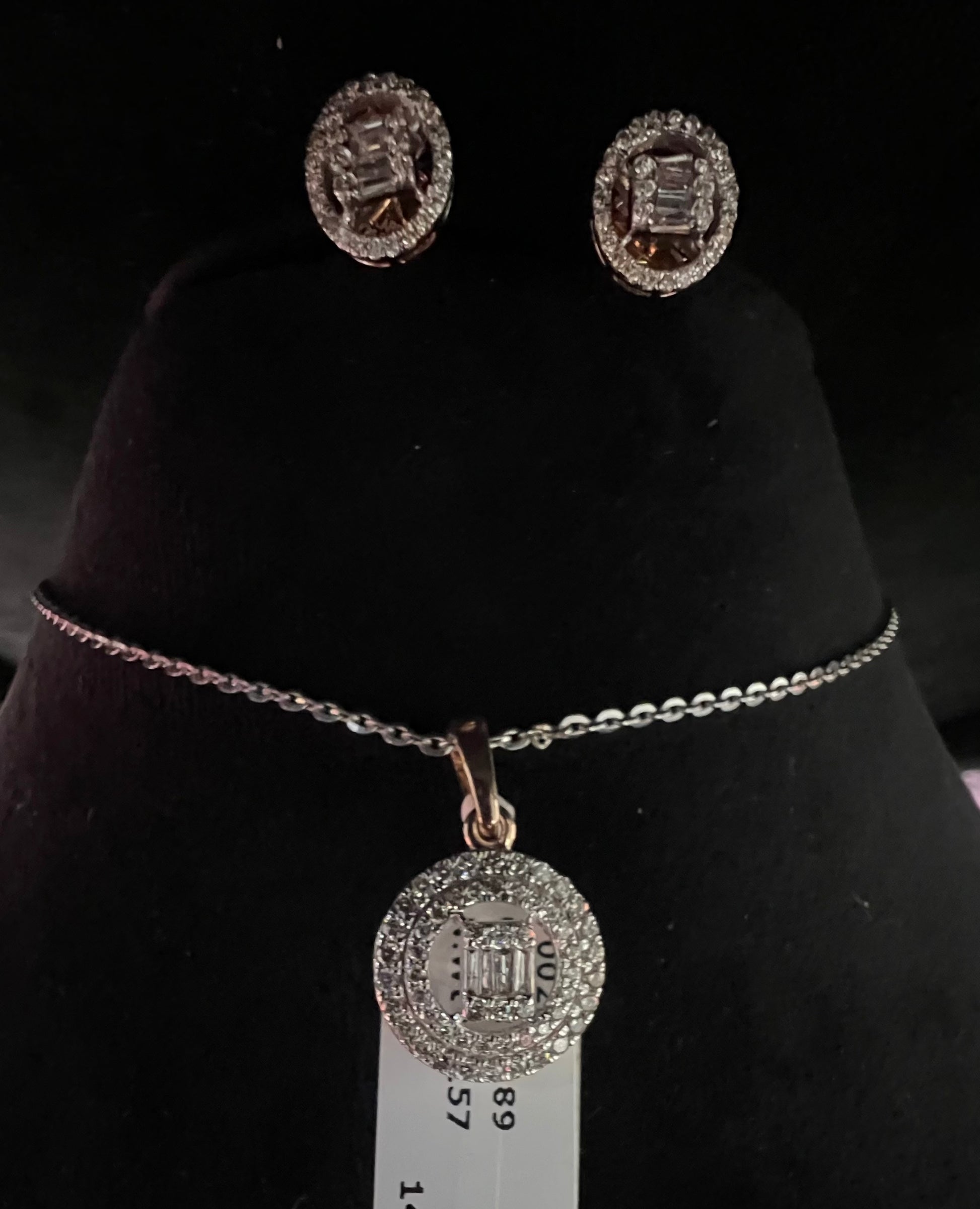 A mannequin showcasing a gold diamond pendant and earrings set, with the pendant hanging from a chain and the earrings displayed above.