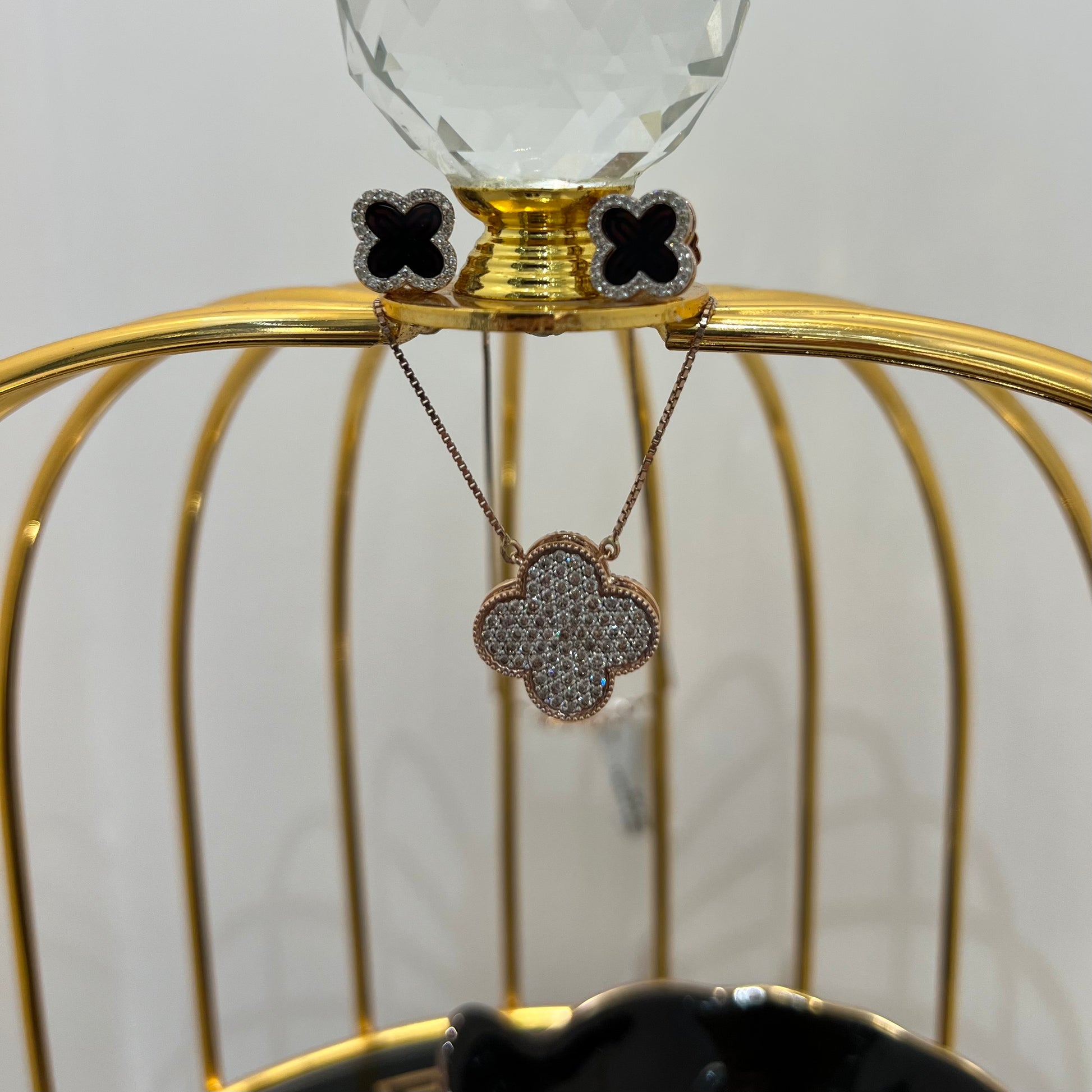 A gold diamond pendant with earrings set, featuring a chain of inset diamonds on a gold-colored metal structure, displayed on a glass stand.