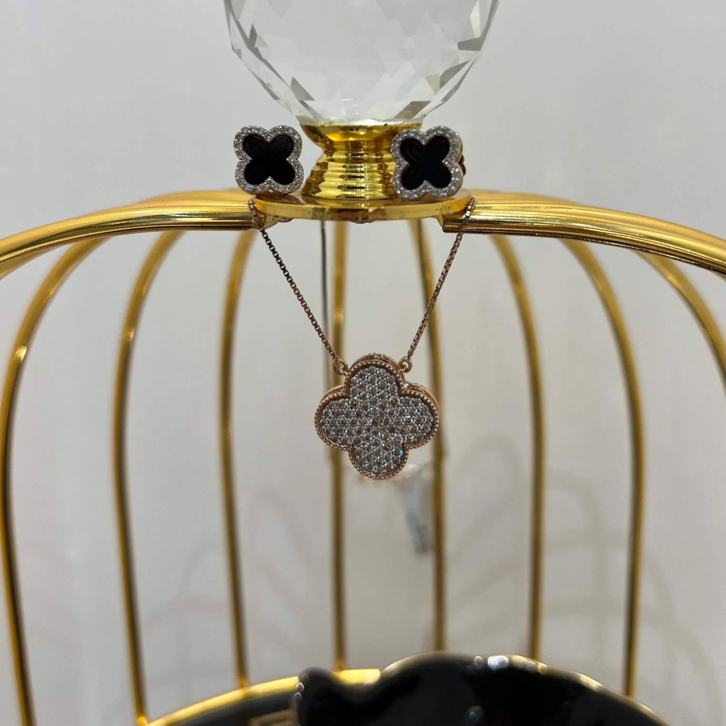 A gold diamond pendant with earrings set, featuring a chain of inset diamonds on a gold-colored metal structure, displayed on a glass stand.