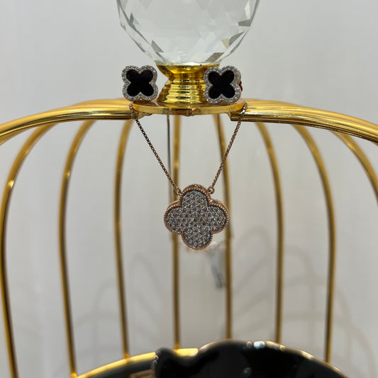 A gold diamond pendant with earrings set, featuring a chain of inset diamonds on a gold-colored metal structure, displayed on a glass stand.